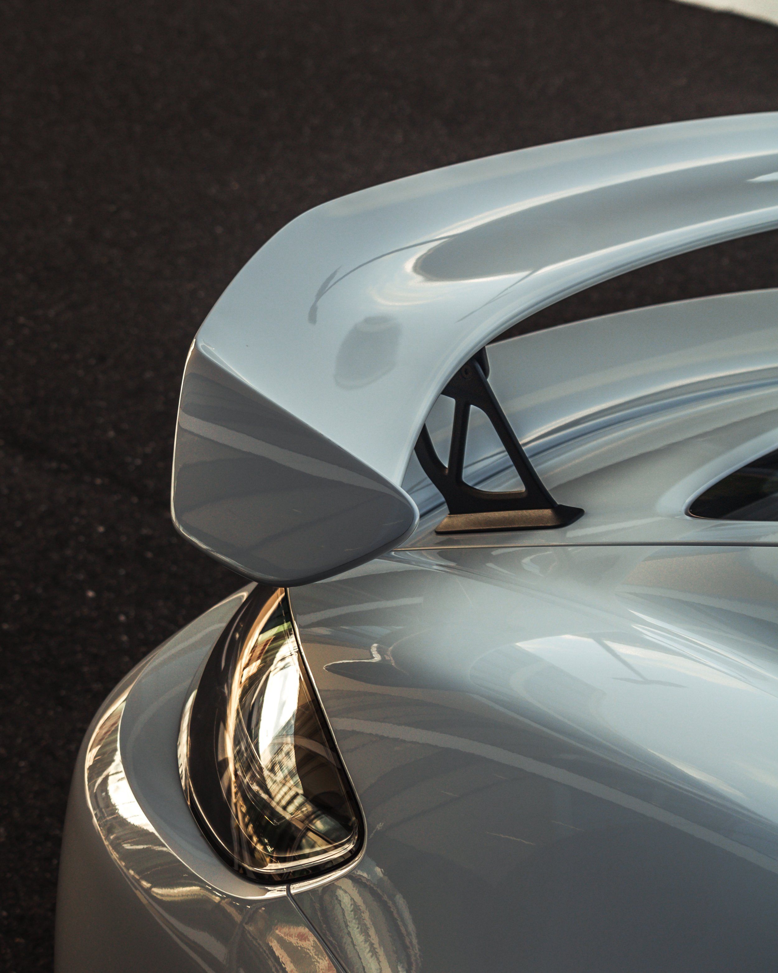 Nahaufnahme eines 718 GT4 auf der Heckseite eines silbernen Sportwagens mit schwarzem Heckspoiler und reflektierendem Scheinwerfer.