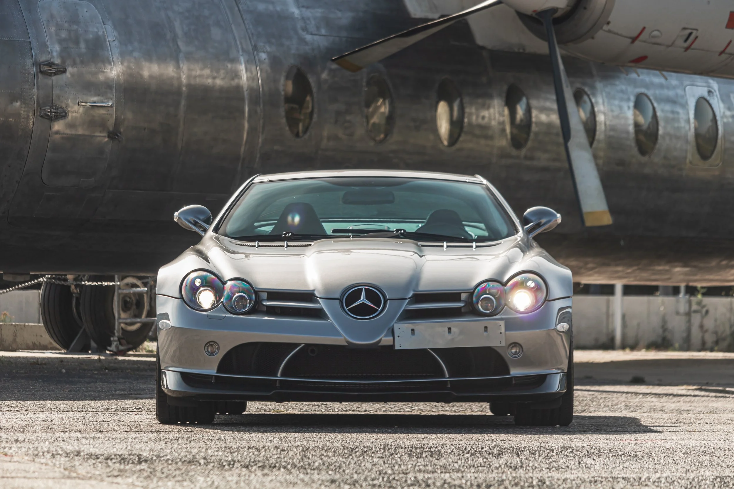 Silberner Mercedes-Benz SLR McLaren vor einem abgestellten Flugzeug