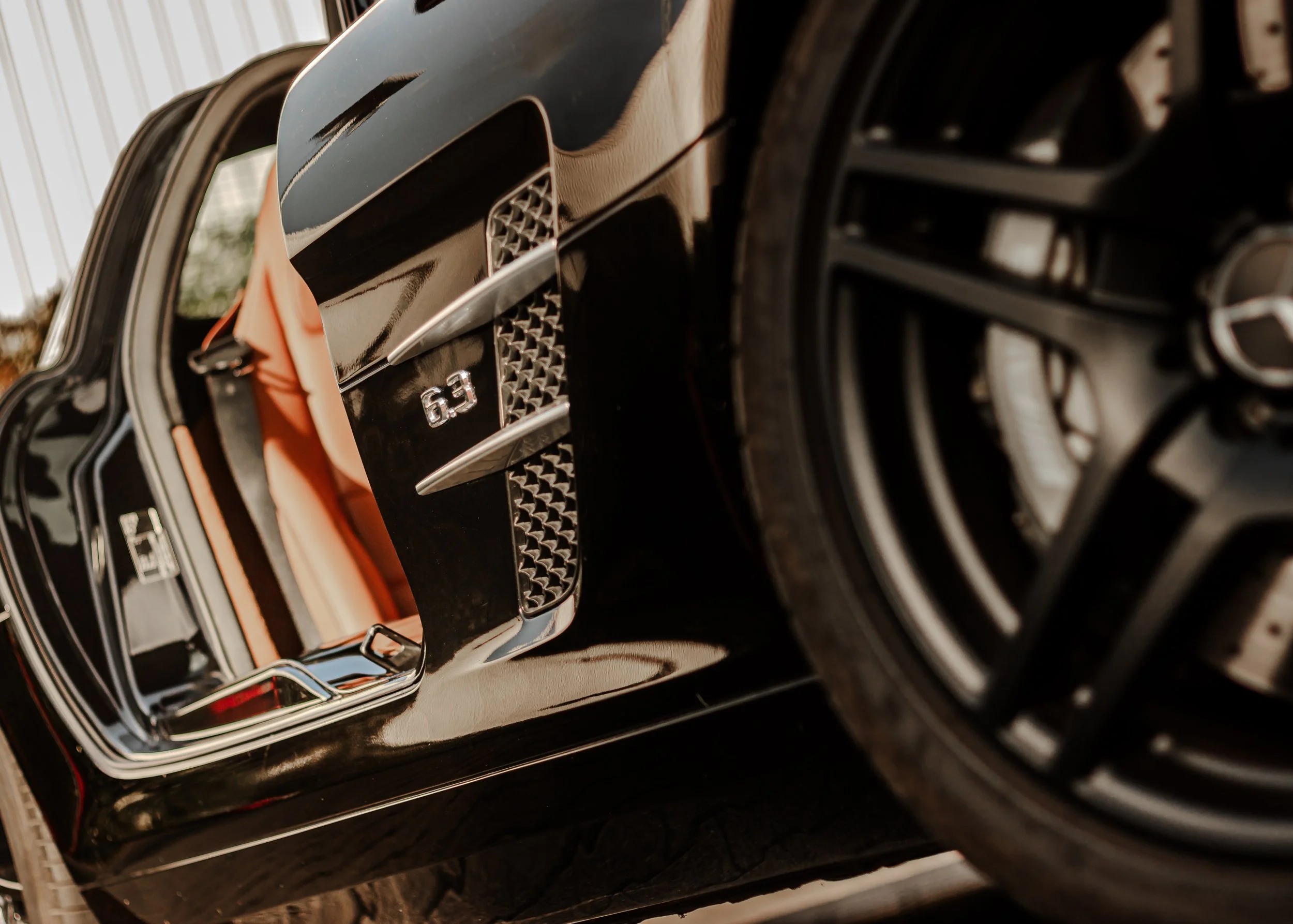 Nahaufnahme eines schwarzen Luxusautos mit Lufteinlässen und einem roten Innenraum, das auf einer Straße parkt.