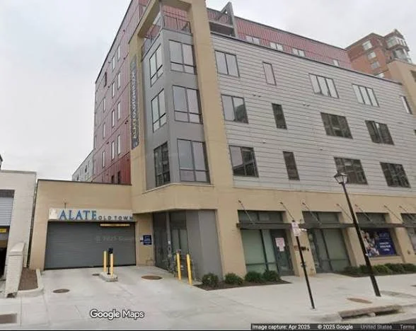 Modern multi-story building with commercial spaces on the ground floor and residential units above, with a street view, street lamps, and a garage door.
