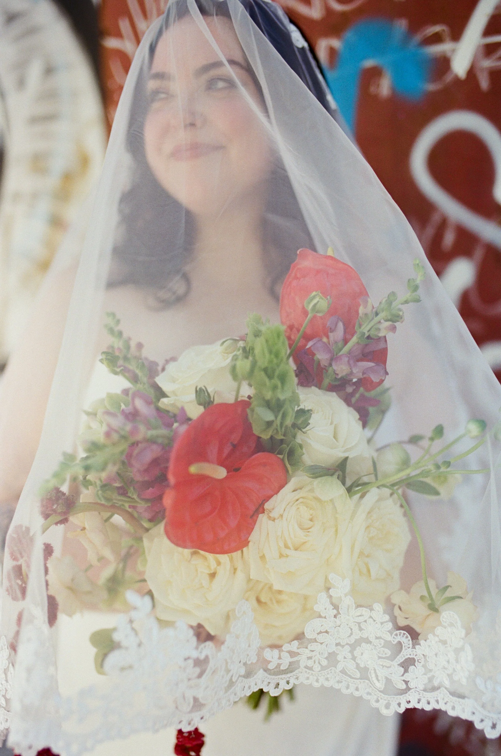 A woman wearing a wedding veil holding a colorful bouquet of flowers.