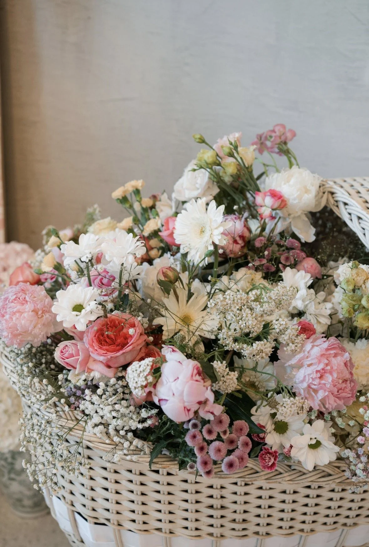 A basket filled with assorted pink, white, and cream flowers, including roses, daisies, and baby's breath, arranged in a decorative display.