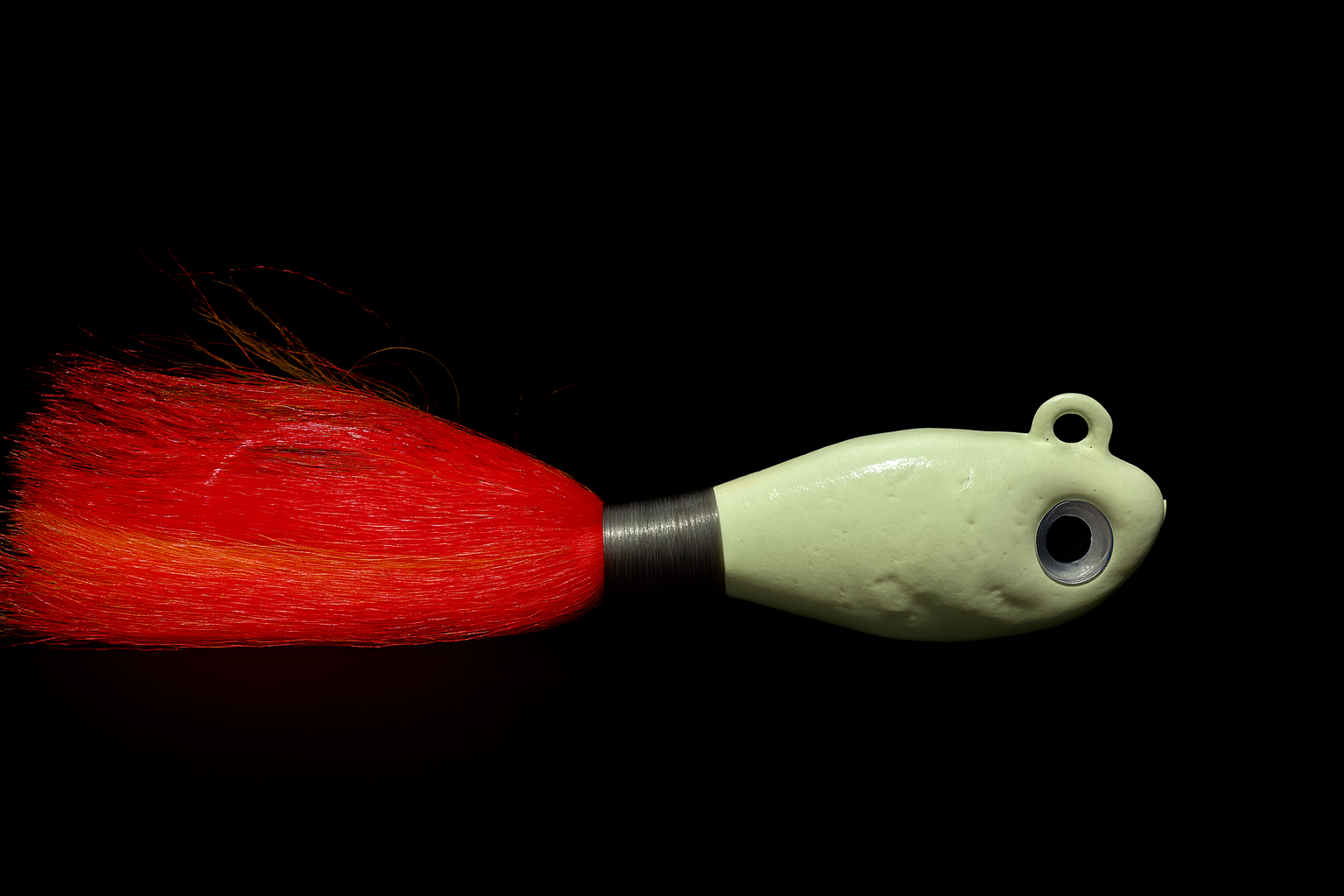 A fishing lure with a white plastic body, a black metal collar, and a red feathered tail against a black background.