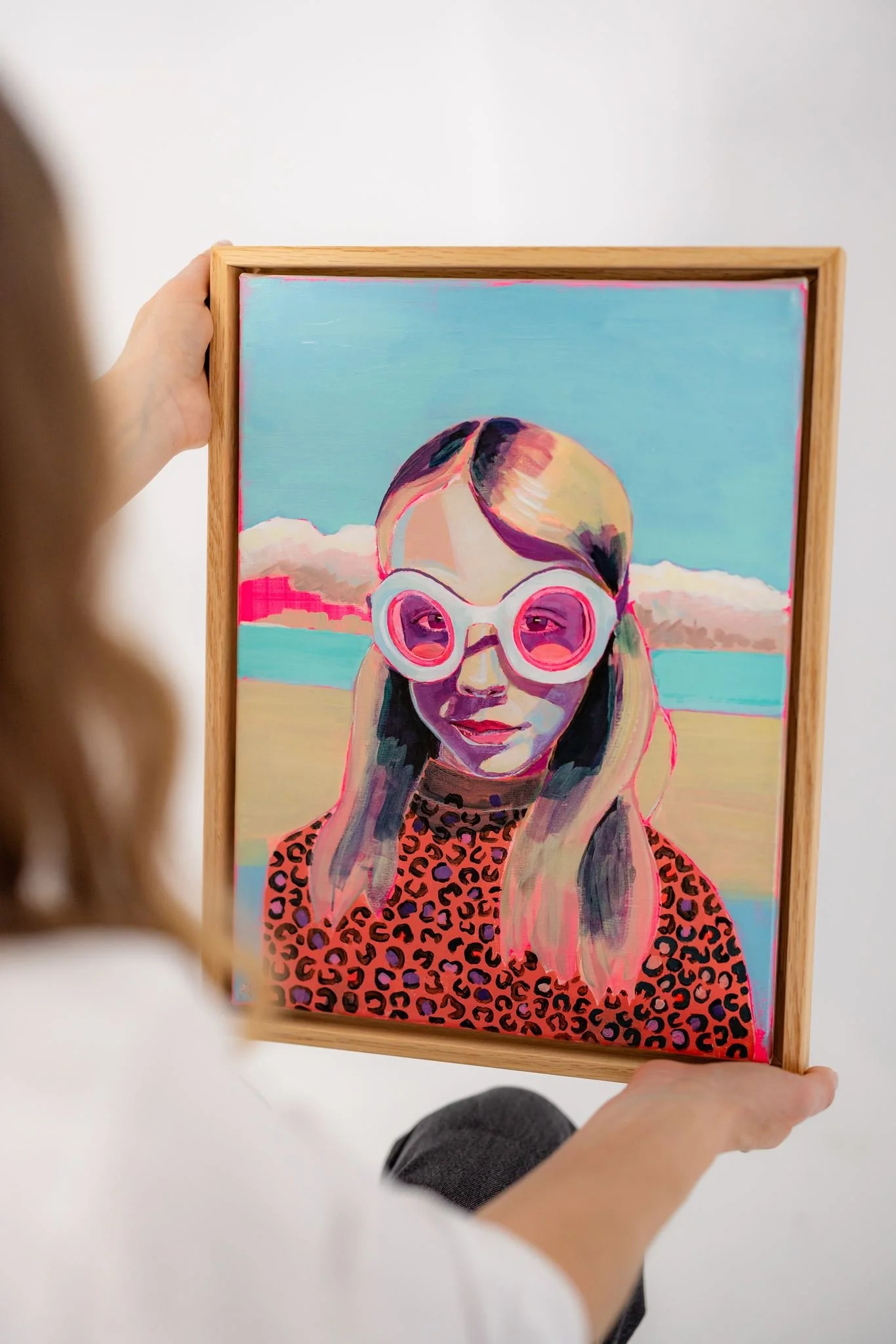 A woman holds a portrait of a child, painted in fluorescent pinks and aqua.