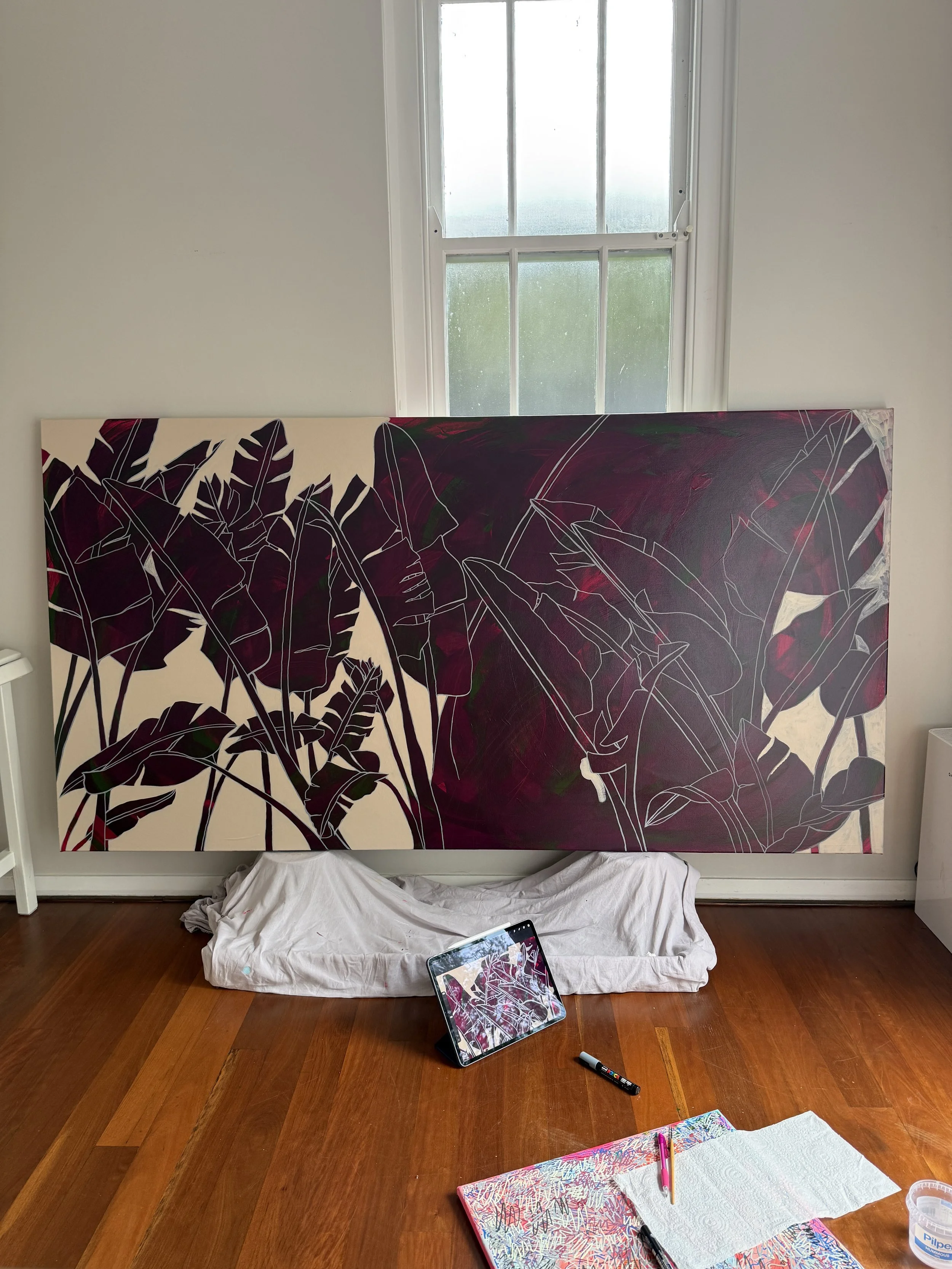 A large scale painting of bird of paradise palms in progress, with an iPad showing a working drawing
