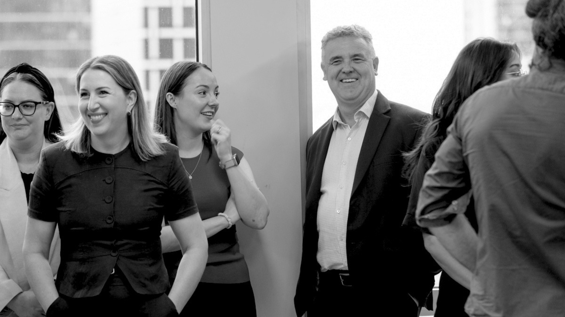 Group of diverse professionals smiling and engaging in conversation in an office setting.