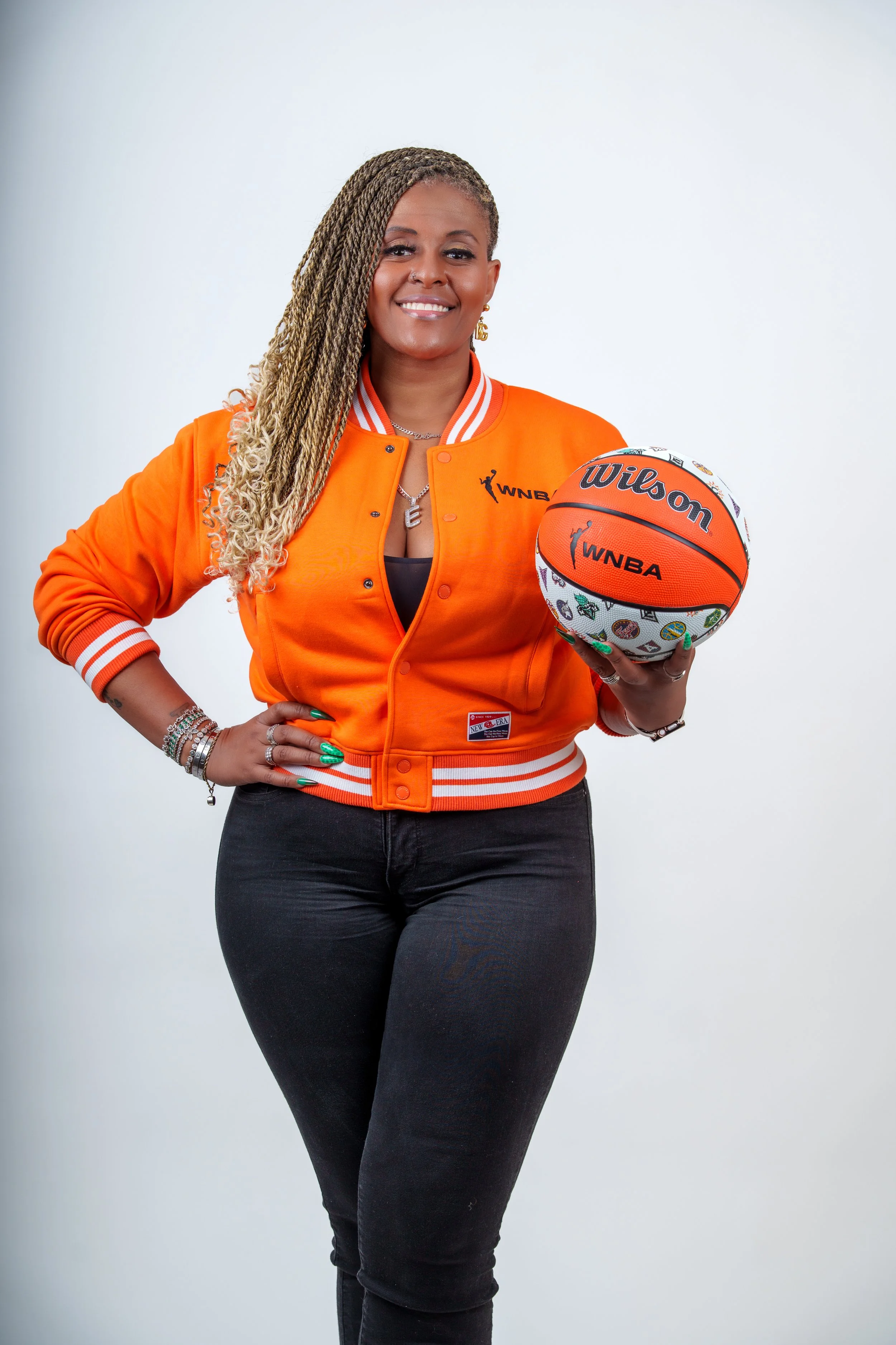 Woman in orange jacket holding a basketball, standing against a plain white background.