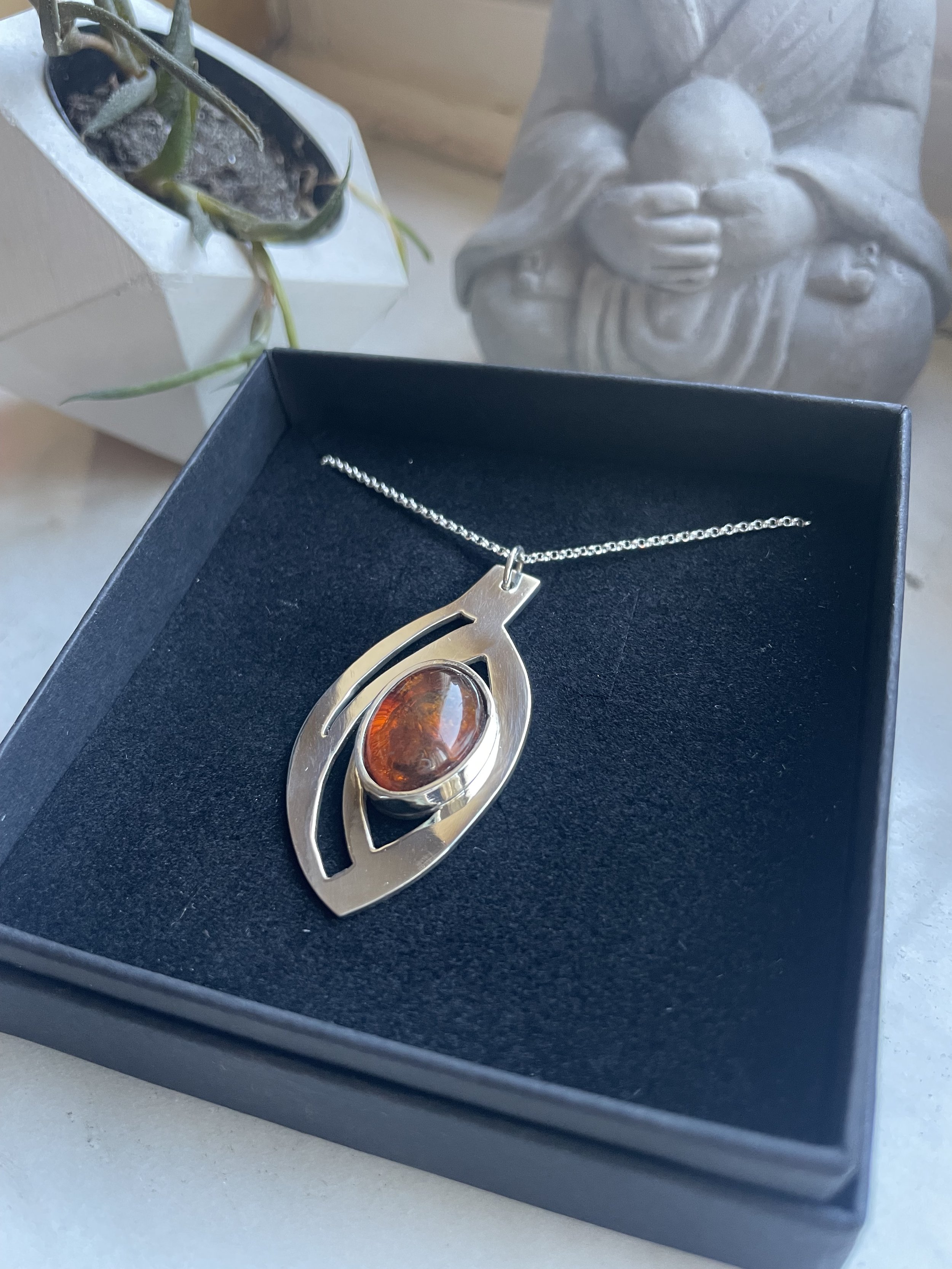 Collana con pendente di forma astratta e una pietra di colore ambra in una scatola nera