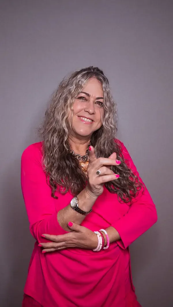 Mujer de cabello rizado con ropa rosa, haciendo un gesto con la mano y sonriendo