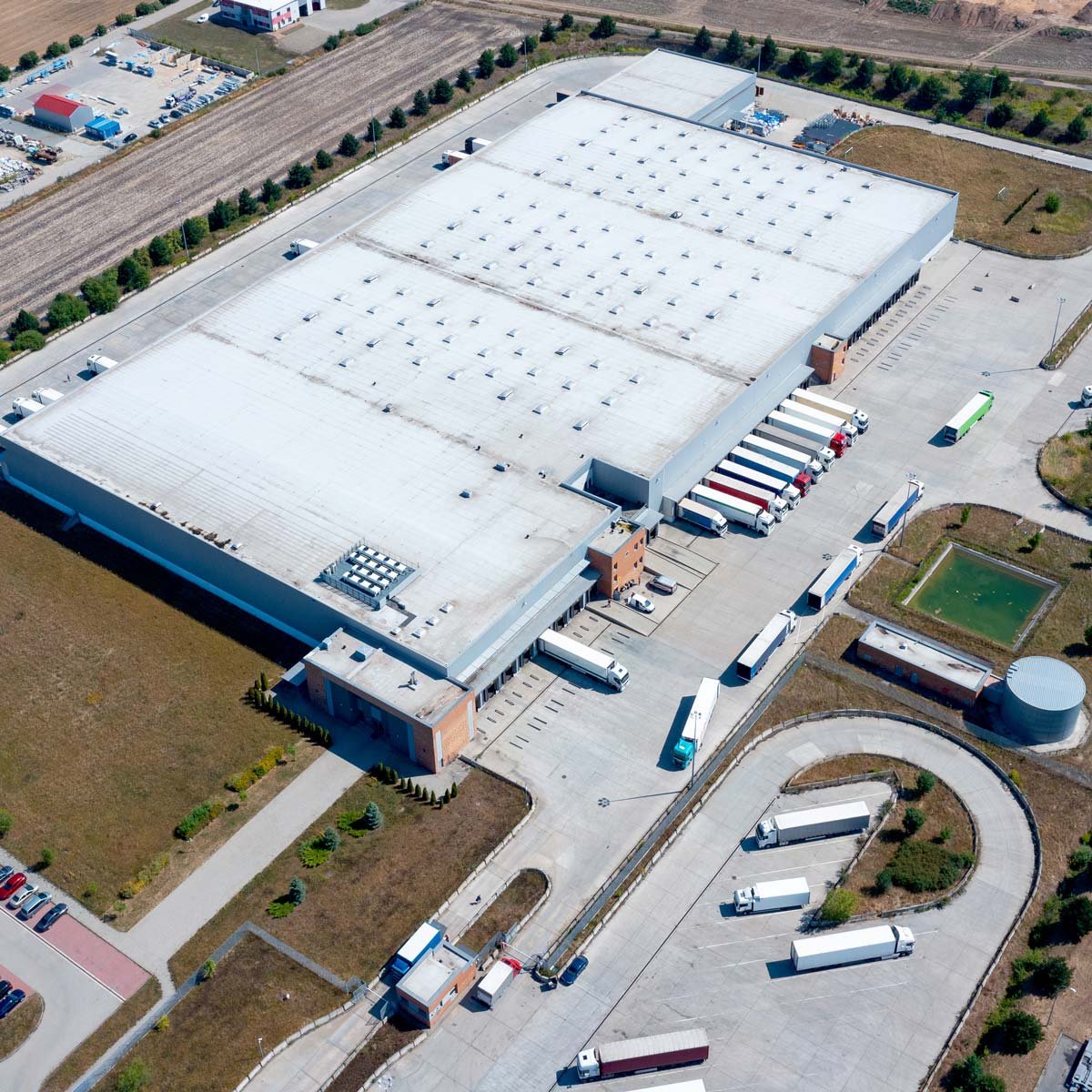 Aerial view of a large industrial warehouse and distribution centre with delivery trucks parked at loading docks and surrounding transport roads