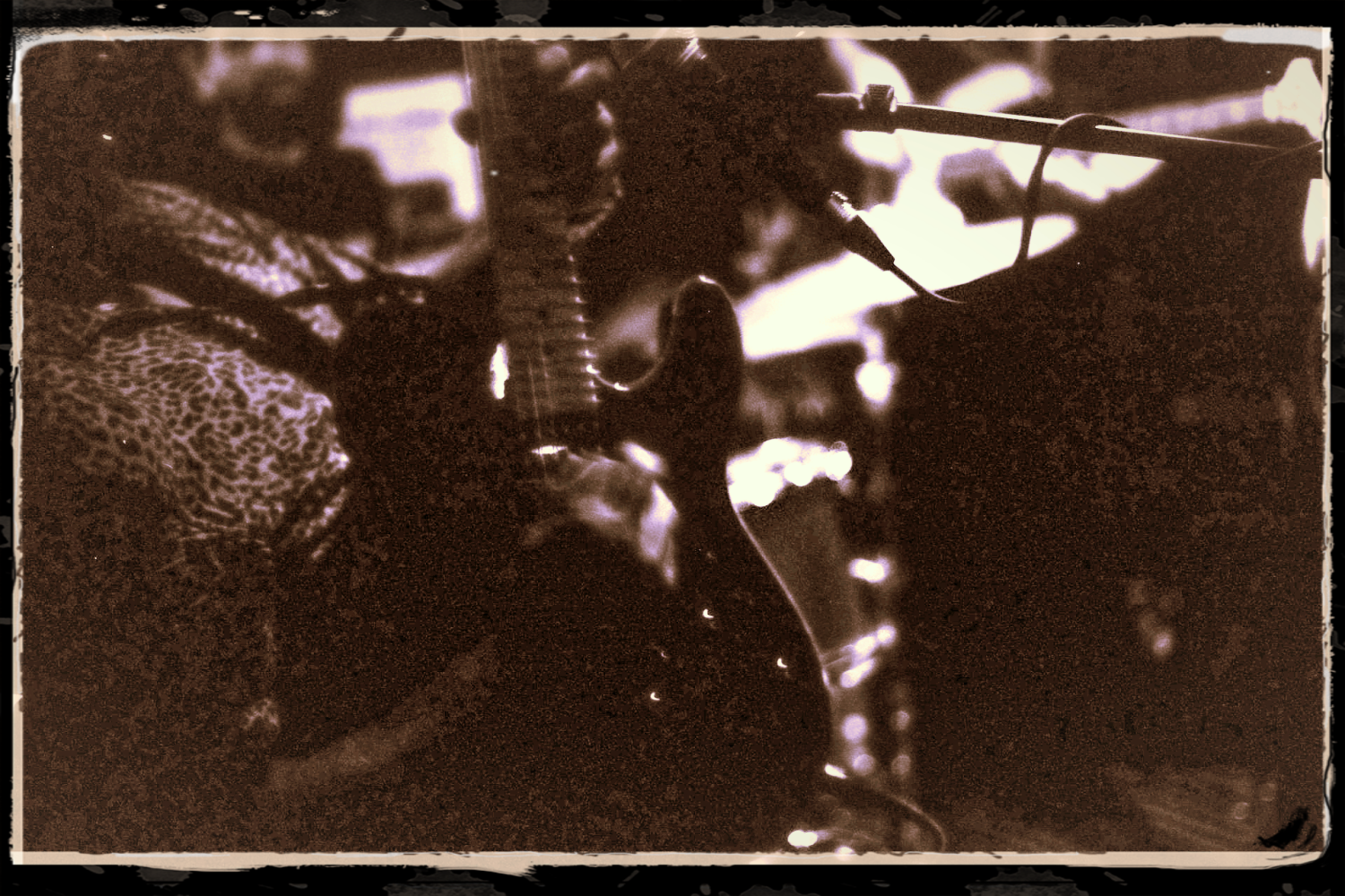 Sepia-toned image of Danny John playing an electric guitar with leopard print clothing, cables in foreground.