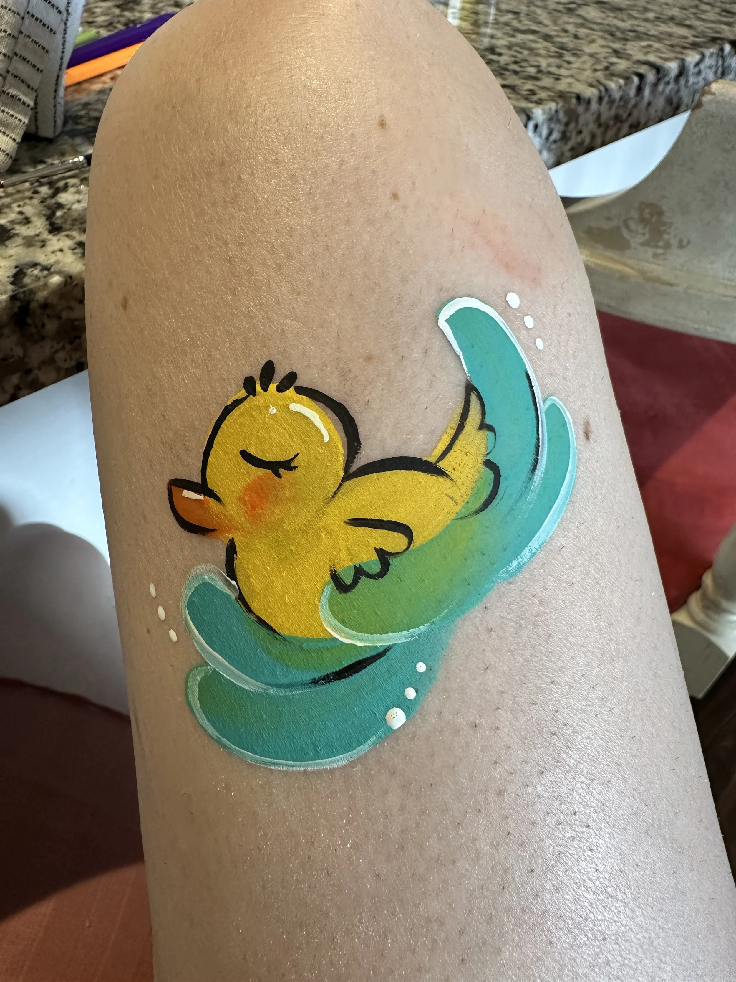 A colorful sticker of a yellow duck with closed eyes, sitting on a green and blue wave.