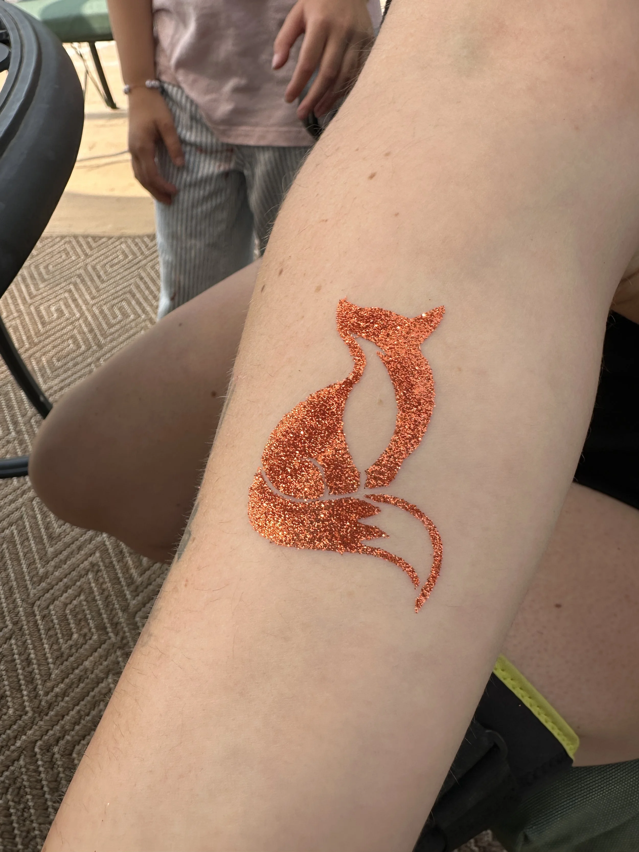 Glittery orange tattoo of a sitting cat on a person's thigh.