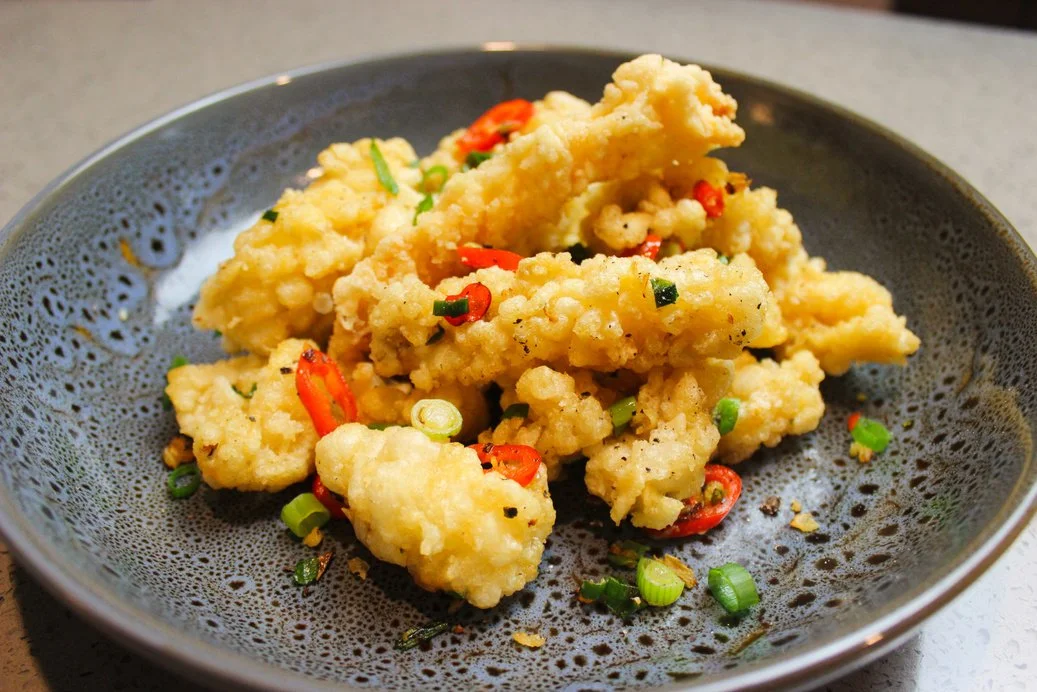 Salt and Pepper squid garnished with sliced red chili peppers and chopped green onions served on a black plate.