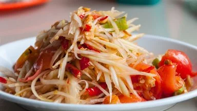 Bowl of Thai papaya salad with shredded green papaya, cherry tomatoes, and chopped herbs
