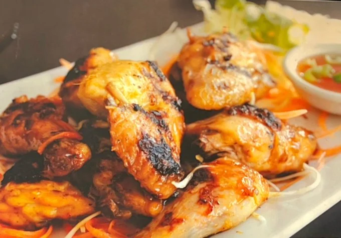 Plate of thai style grilled chicken with a side of shredded lettuce and a small bowl of dipping sauce.