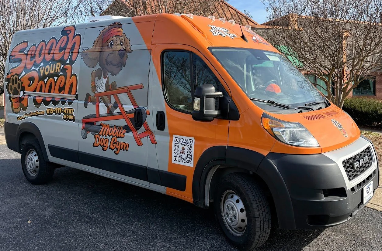 Orange and gray mobile dog gym van with cartoon dog mascot, paw prints, and QR code parked on street.