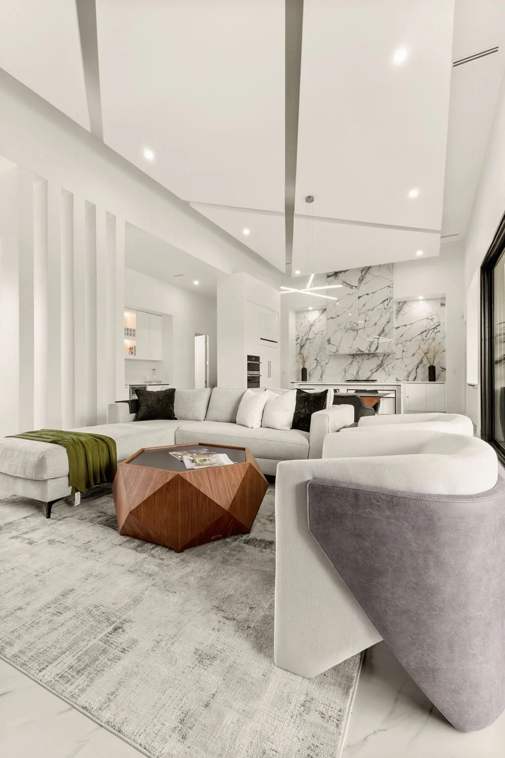 Modern living room with light-colored sectional sofa, patterned rug, wooden coffee table, and marble accent wall in a bright open-concept space.
