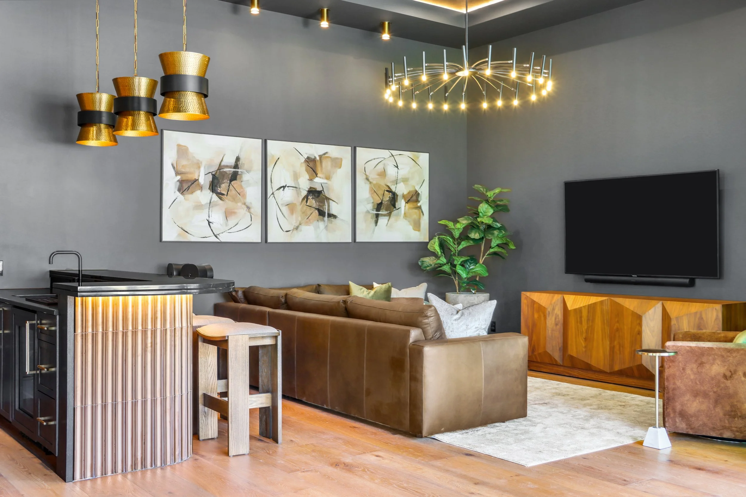 Modern living room with abstract artwork, brown leather sofa, flat-screen TV, green potted plant, and contemporary chandelier.