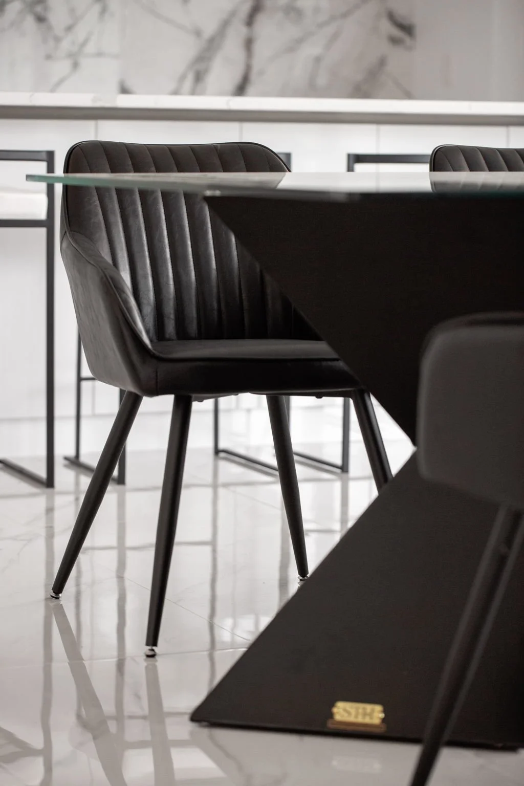 A modern dining room with black leather chairs around a glass-top table, with a white and gray marble wall in the background.