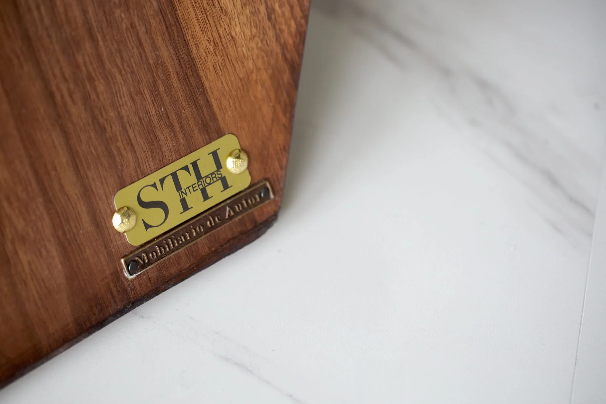 Close-up of a wooden interior sign with a yellow and black label that reads 'STILL INTERIORS' and a small metallic plaque below that says 'Furniture de Autor'.