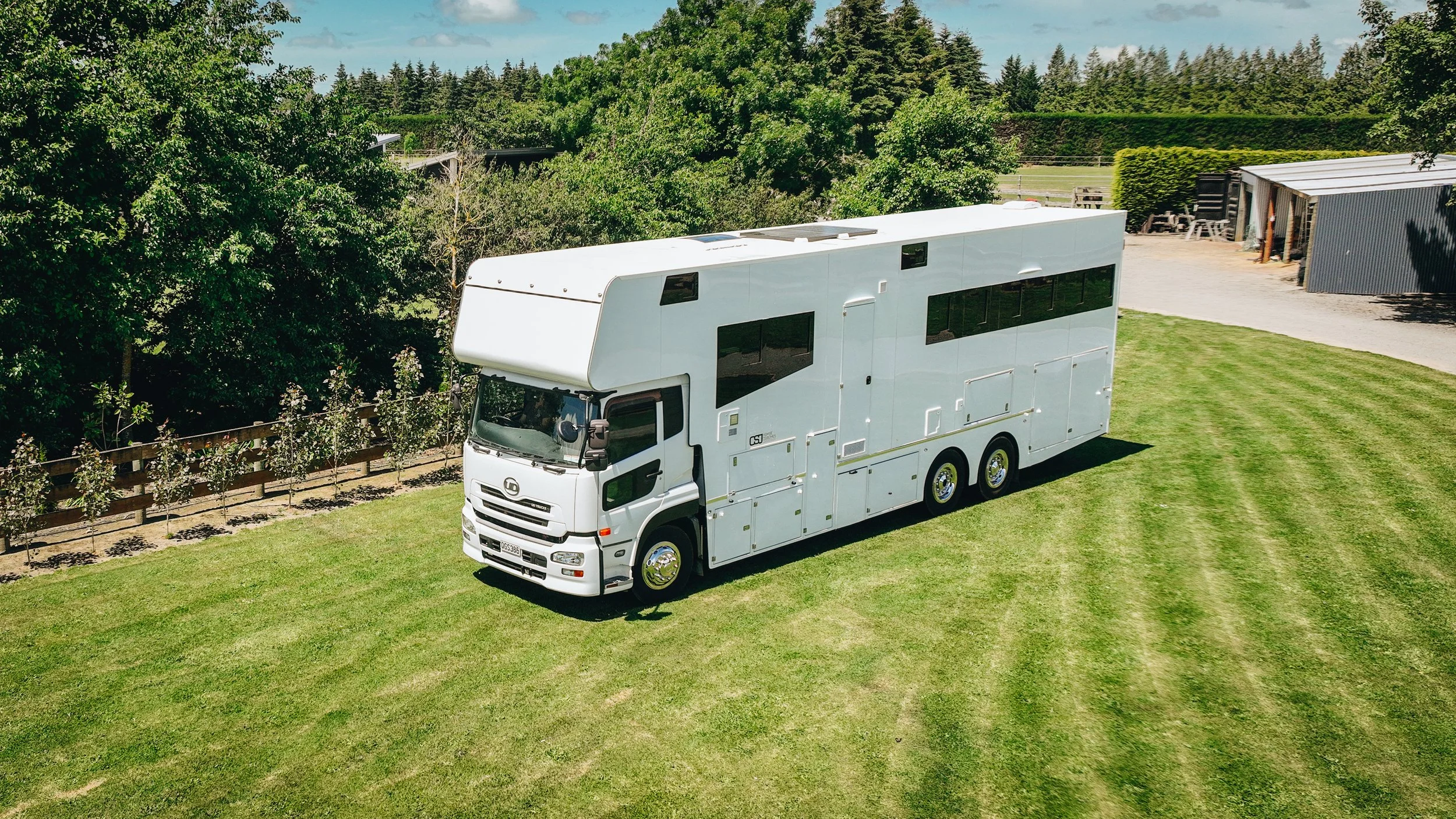 A large white recreational vehicle (RV) parked on a well-maintained grassy area with trees and structures in the background.