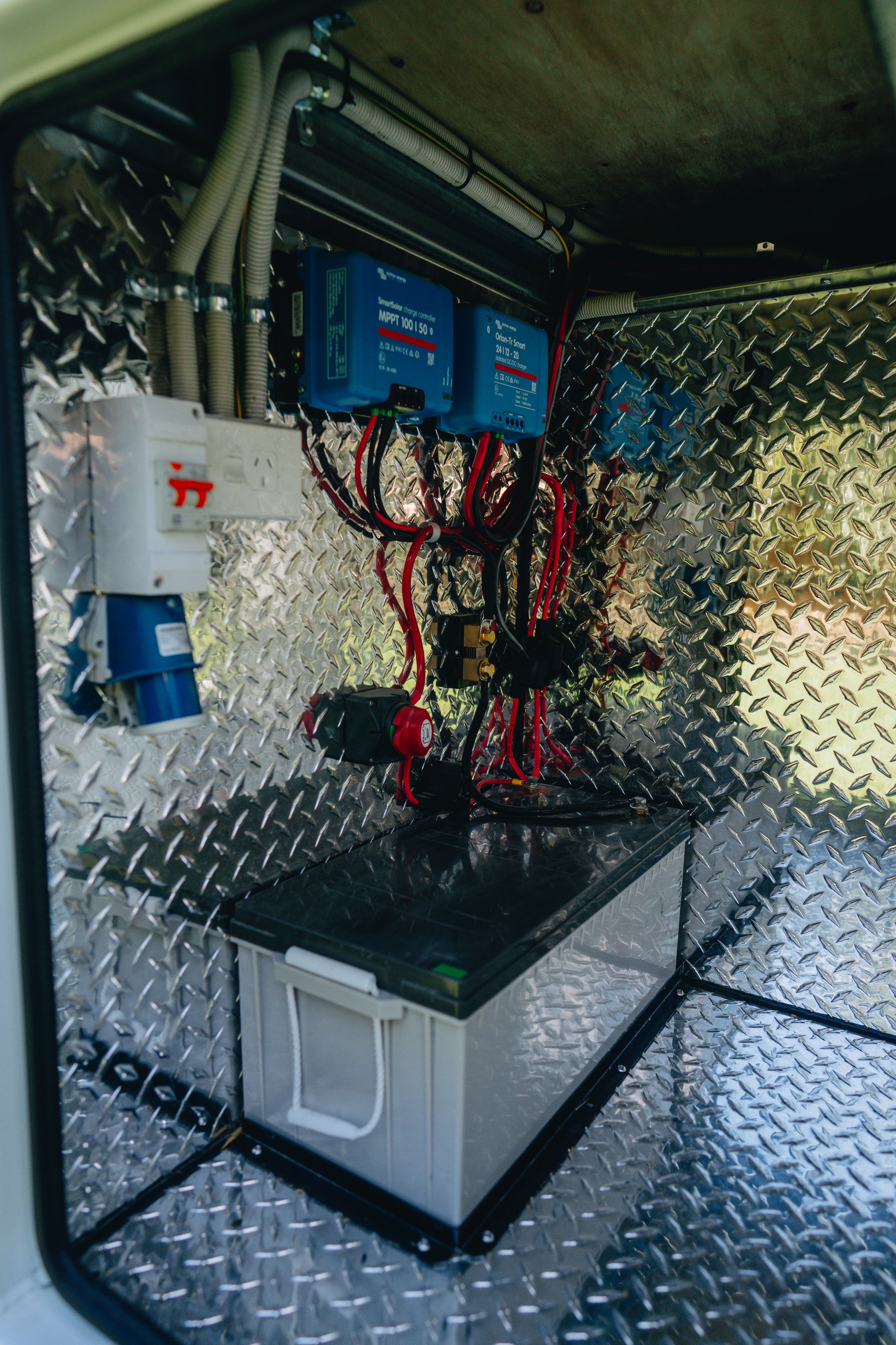 Electrical control panel with wiring, circuit breakers, and batteries on a diamond plate wall.