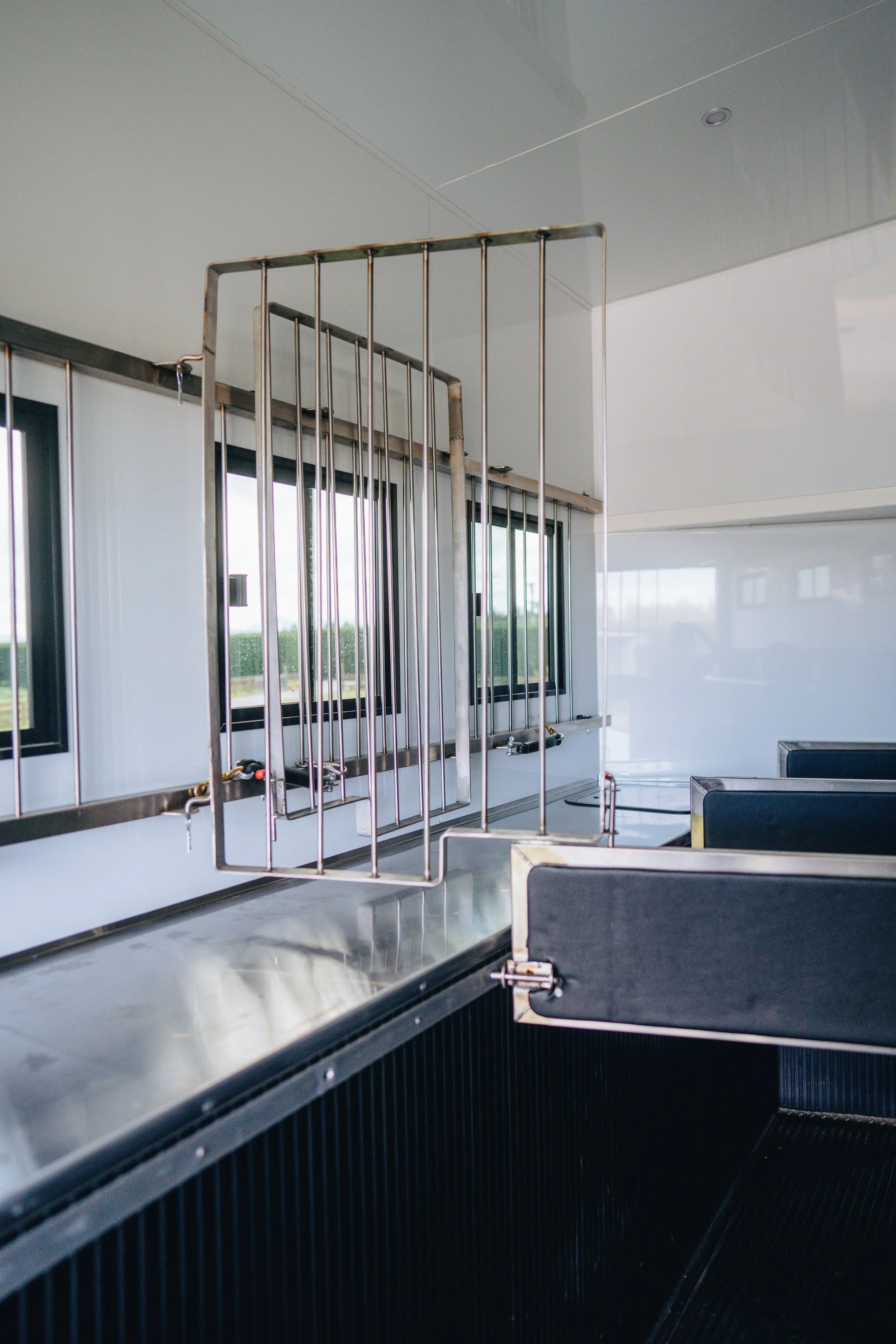 Empty hospital or medical facility patient lift with metal platform and vertical rails, shown beside windows and seating area.