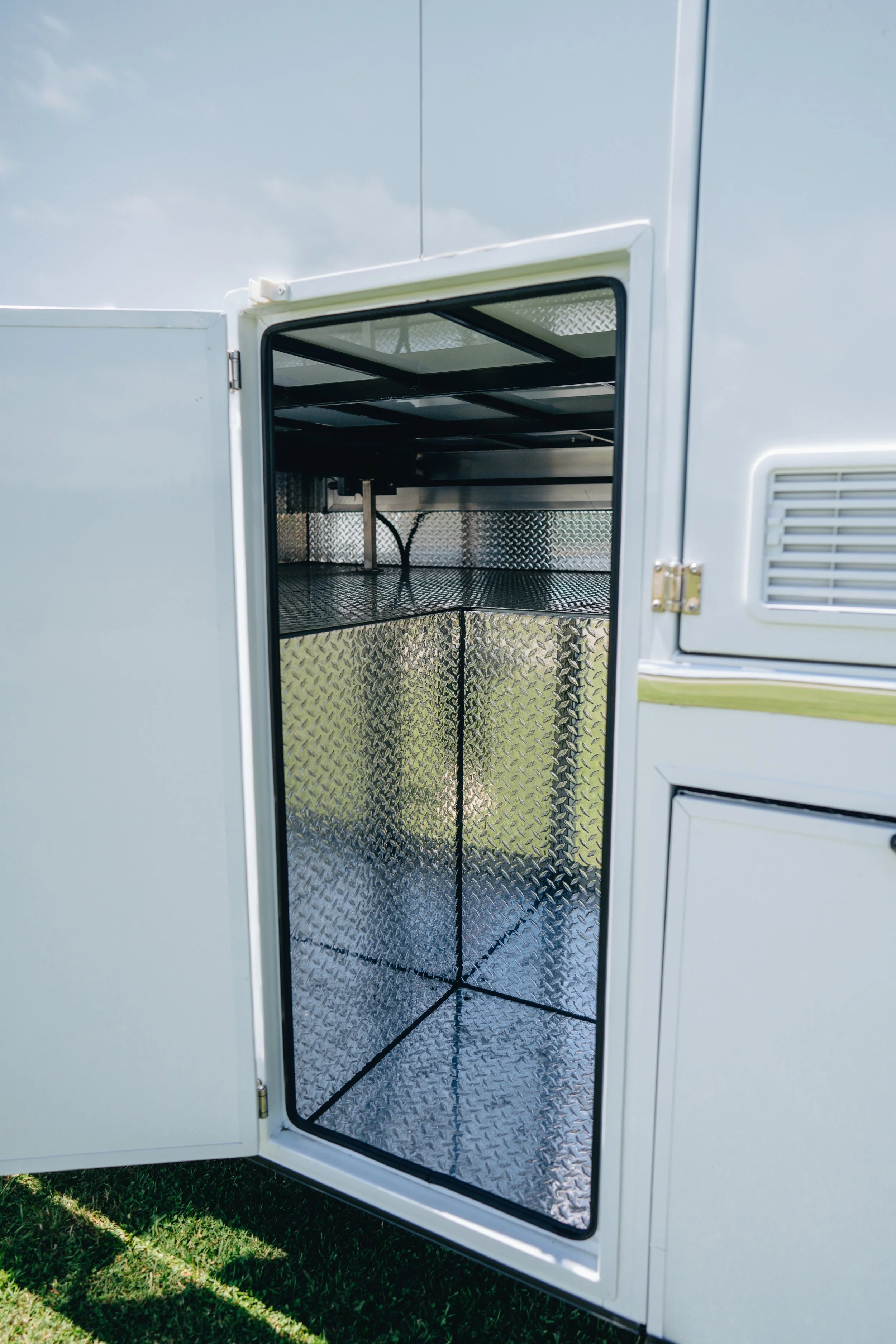 Inside of an open white utility vehicle or trailer with diamond plate interior panels and a metal shelf.