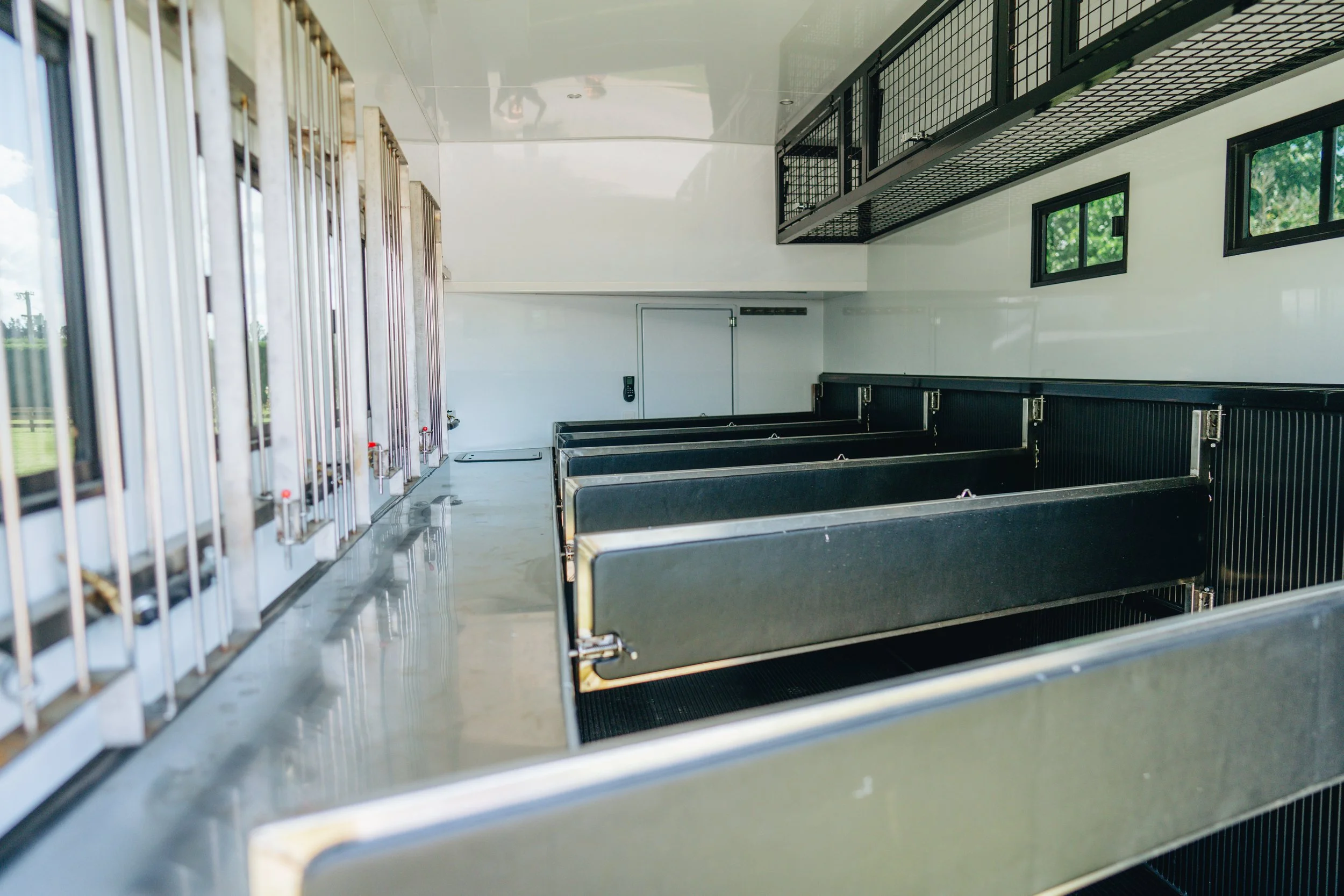 Empty black horse stalls inside a stable trailer with windows and metal dividers.