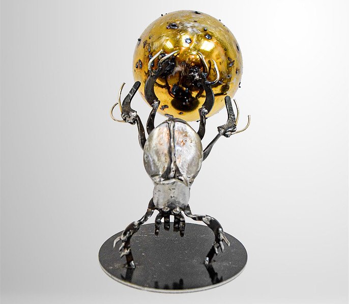 Metal sculpture of a beetle holding a golden orb