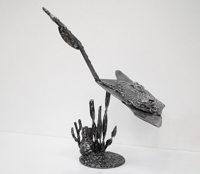 Metal sculpture of a stingray swimming above aquatic plants on a stand