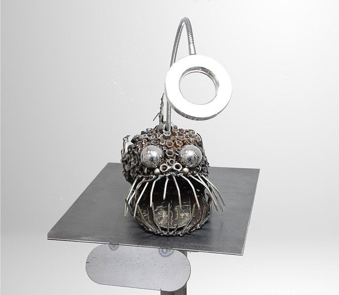 Sculpture of an anglerfish made from metal parts on a stand.
