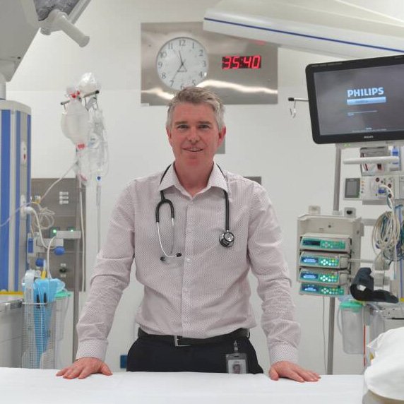 A male doctor standing in a hospital room with medical equipment and monitors