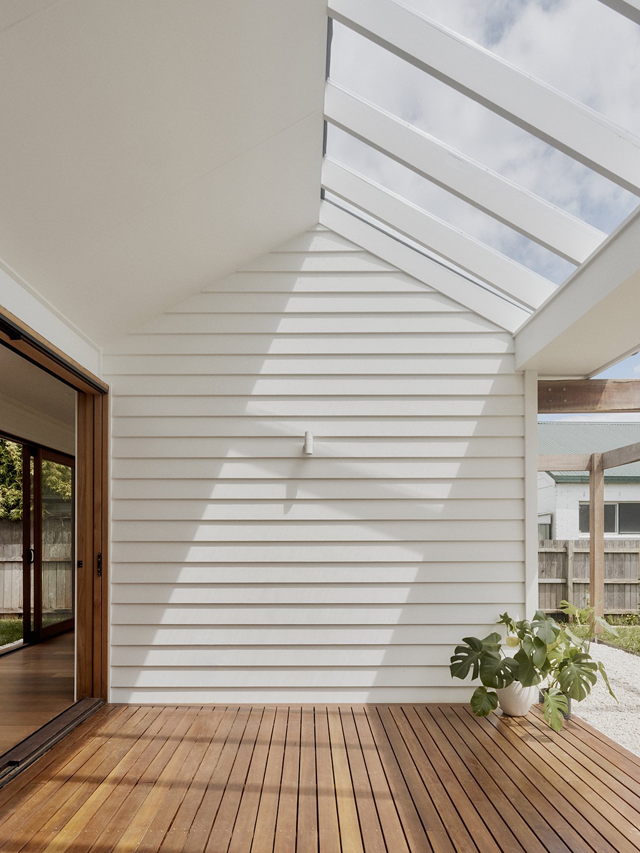 Oversized sun-deck skylight drawing winter sun onto the timber deck, white weatherboard and monstera plant below
