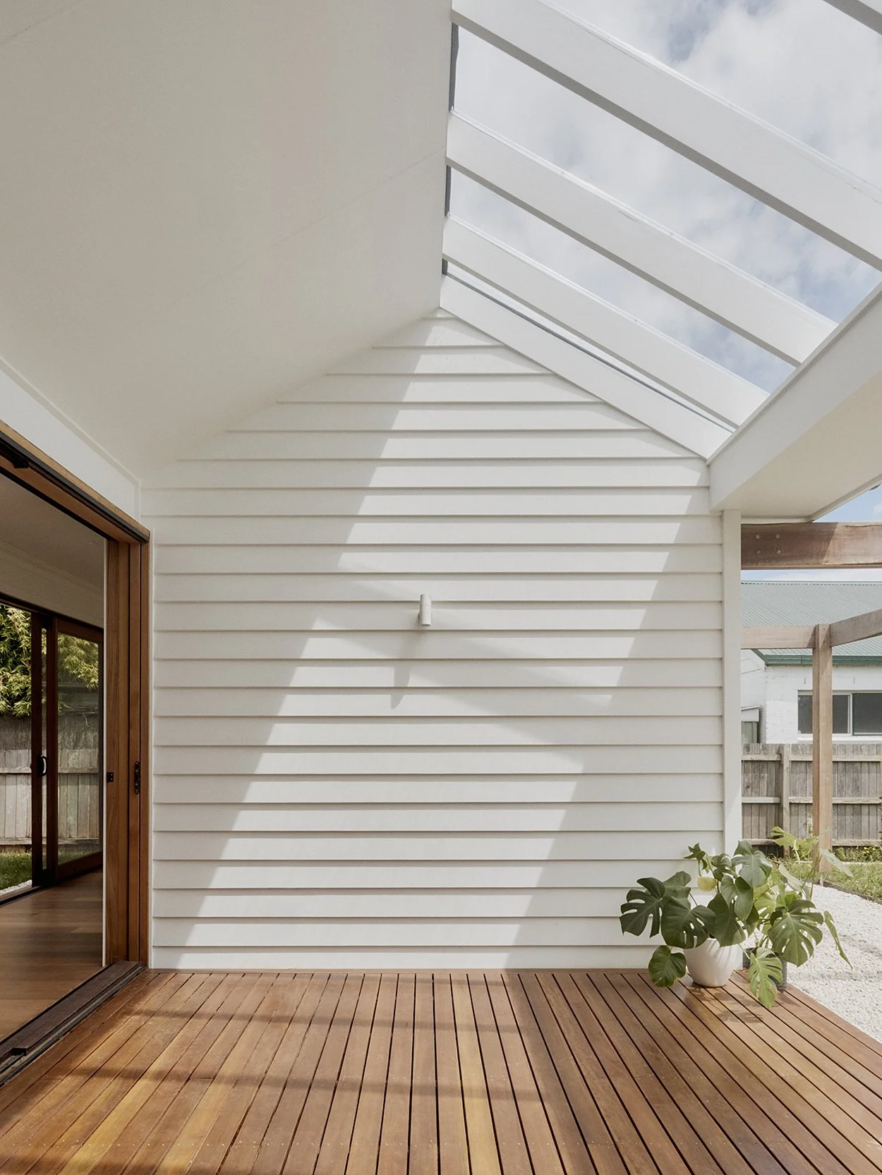 Oversized sun-deck skylight drawing winter sun onto the timber deck, white weatherboard and monstera plant below