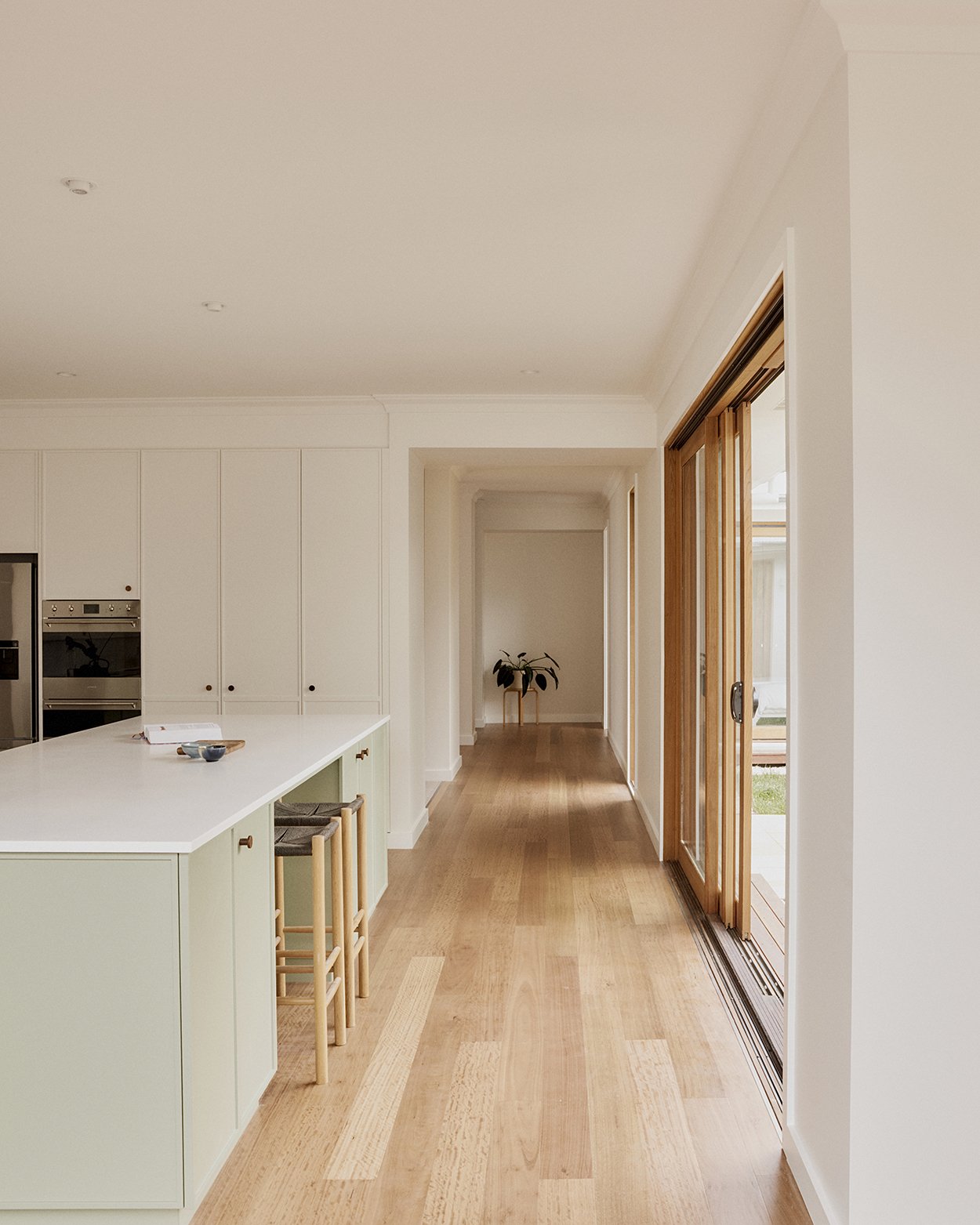 Kitchen and hallway interior with sage green island bench, timber floor and long view through to the rear garden