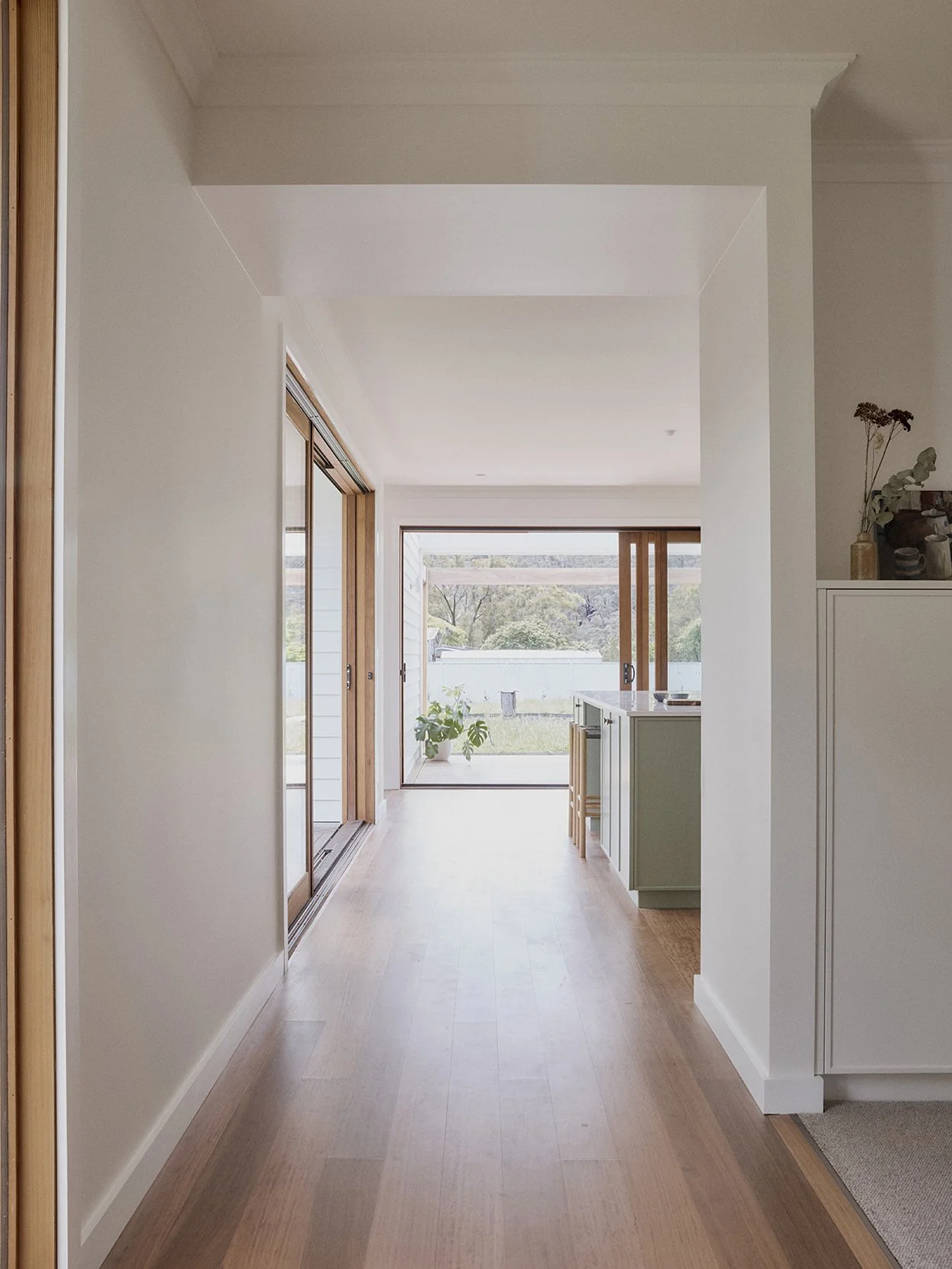 Generous hallway drawing light from the north-facing garden, with sage green kitchen bench visible to the right