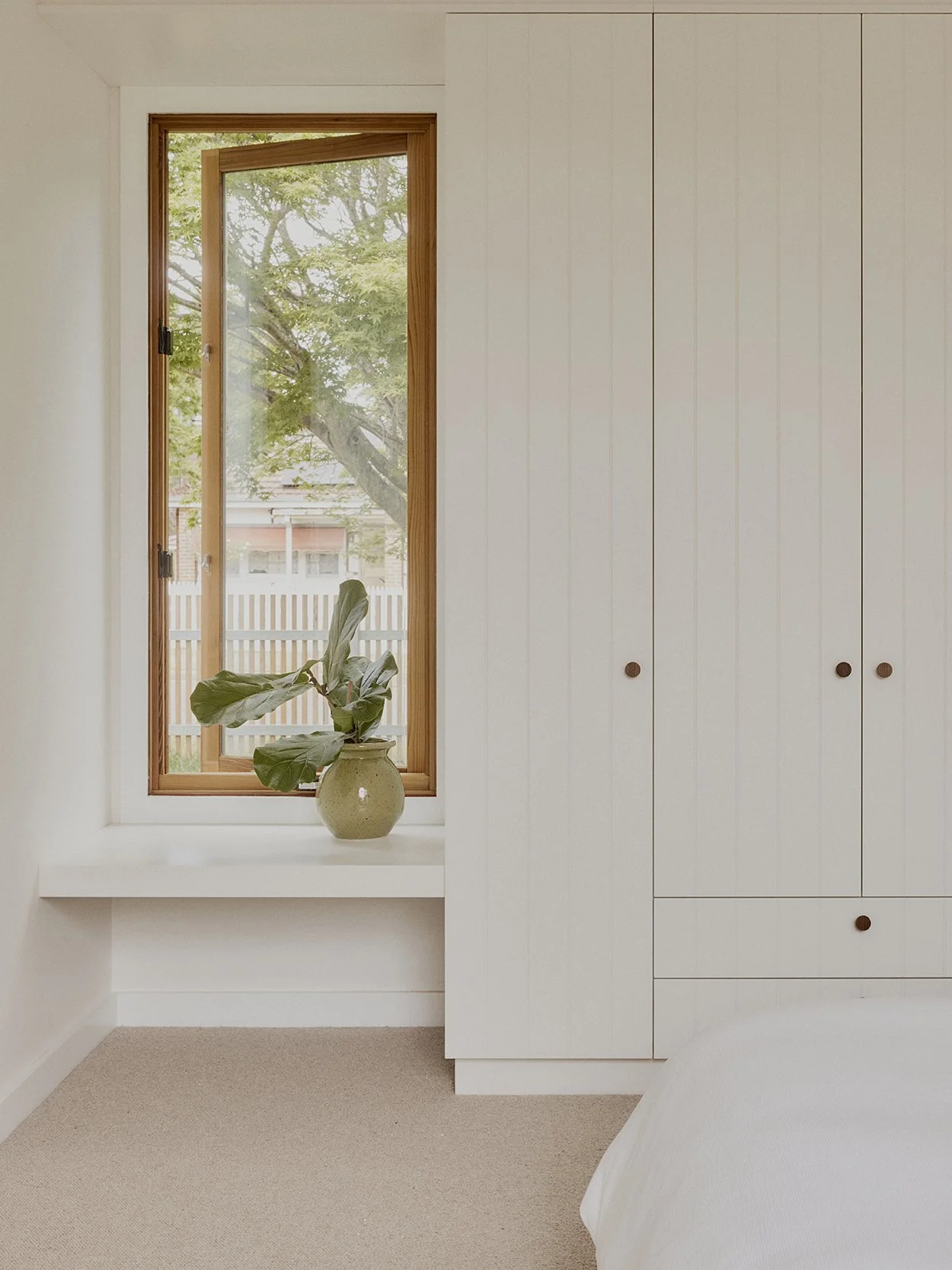 Bedroom interior with built-in wardrobe, integrated window shelf and timber-framed window overlooking the garden