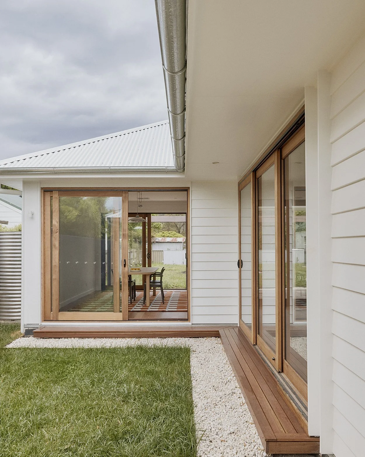 Private courtyard with timber deck, white gravel and lawn connecting to living areas via timber-framed sliding doors