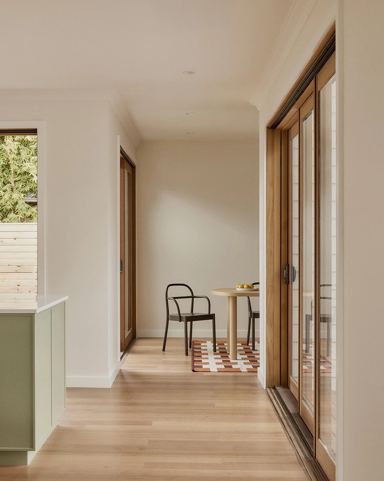 View from kitchen toward dining area with patterned rug, round table and timber-framed sliding door to garden