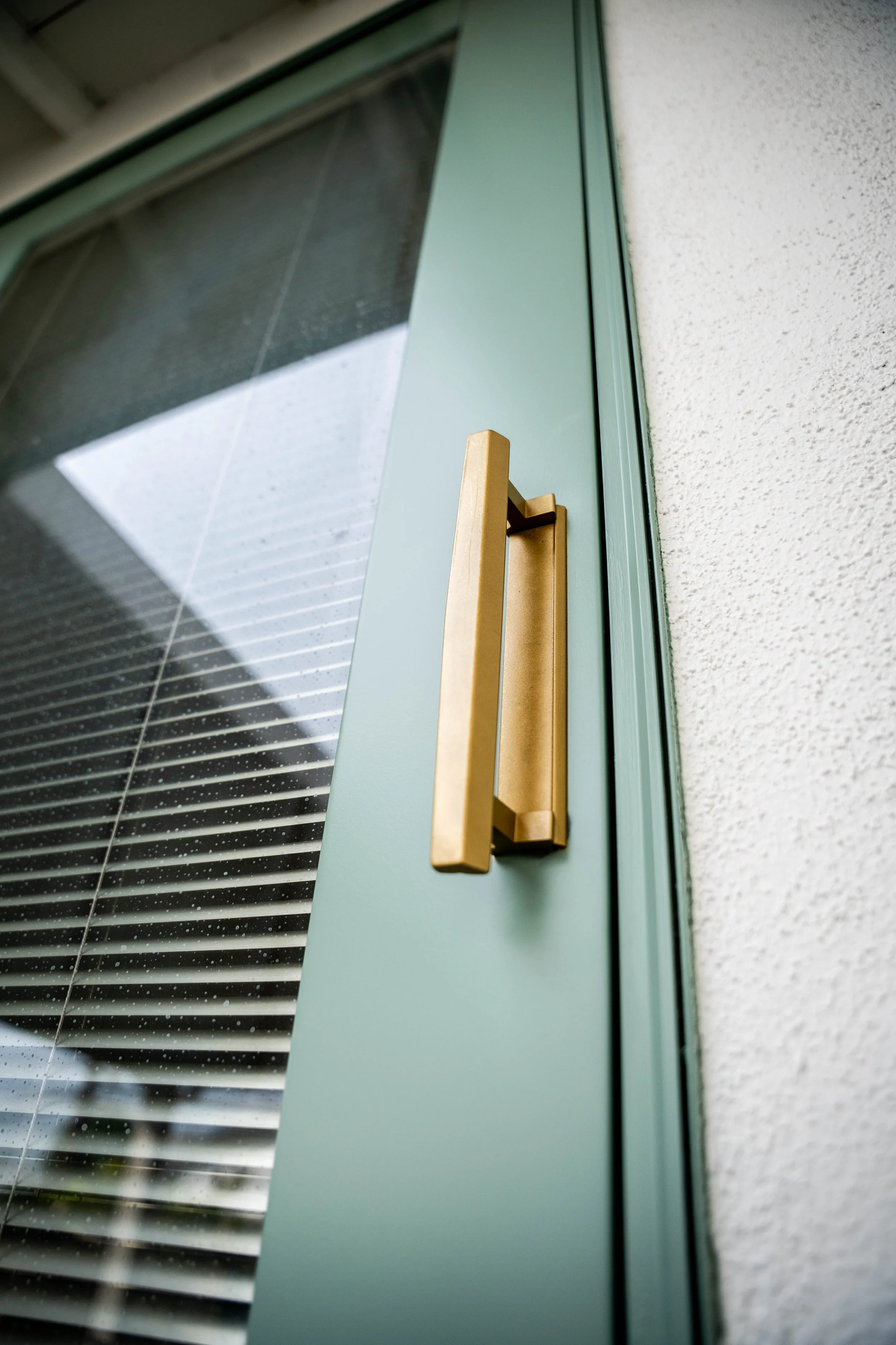 Close-up view of a modern green door with a gold handle and a textured white wall on the right.