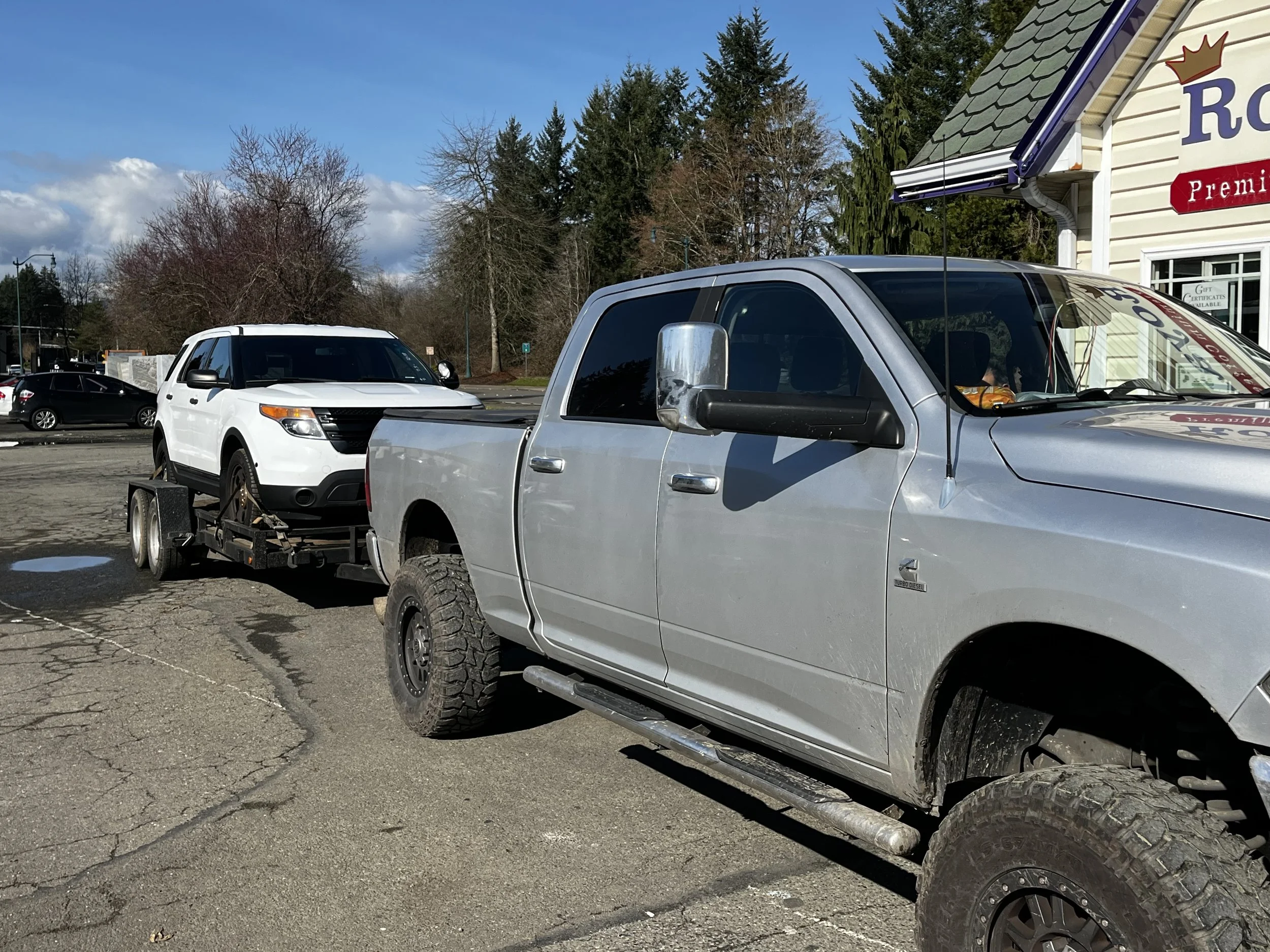 Gray pickup truck towing white SUV on a trailer in a parking lot.