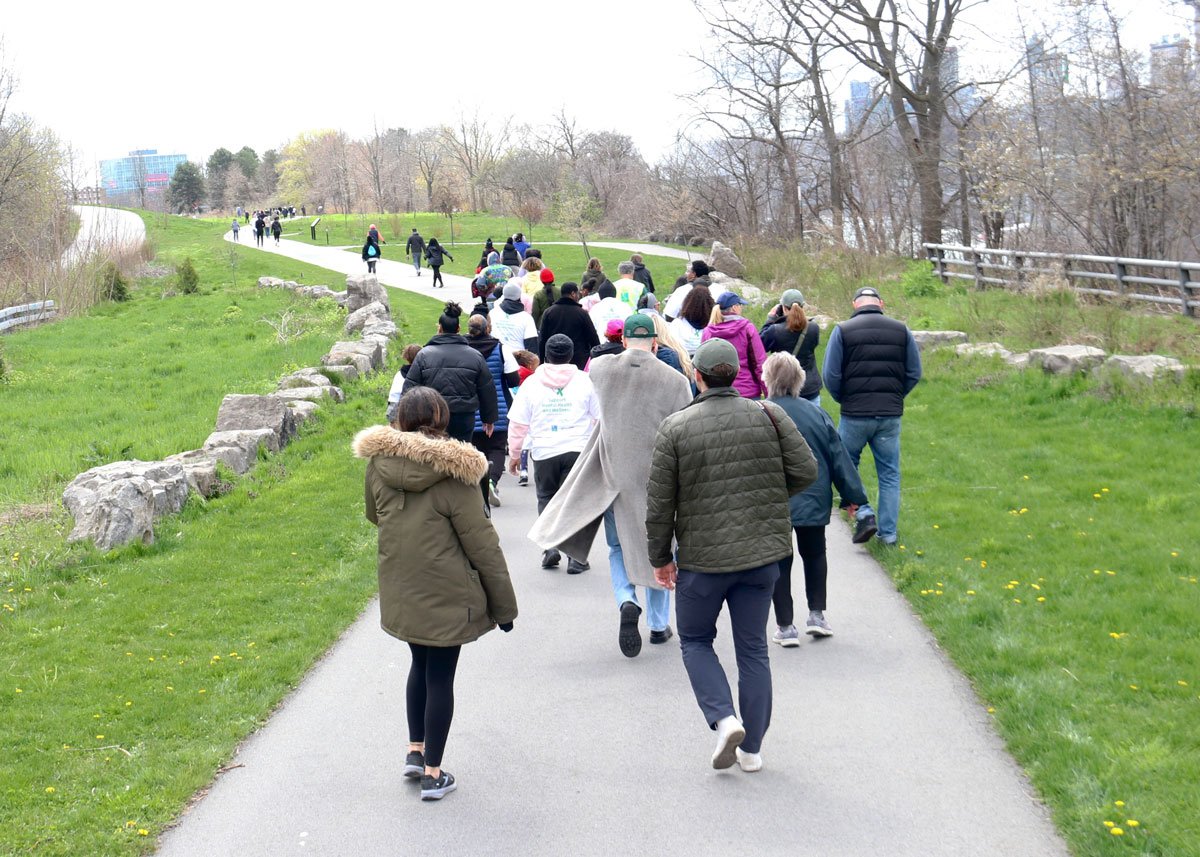A group of people walking along a paved pathway through a park.