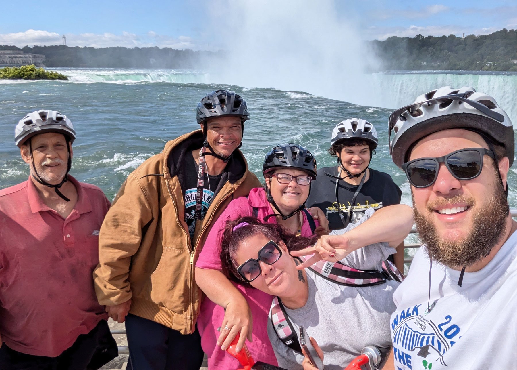 Group of six people wearing helmets taking selfie at Niagara Falls with the waterfall in the background.