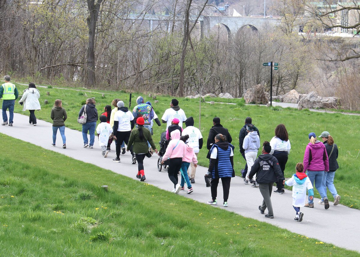 Group of people walking along a paved path in a park, with trees and rocks in the background.