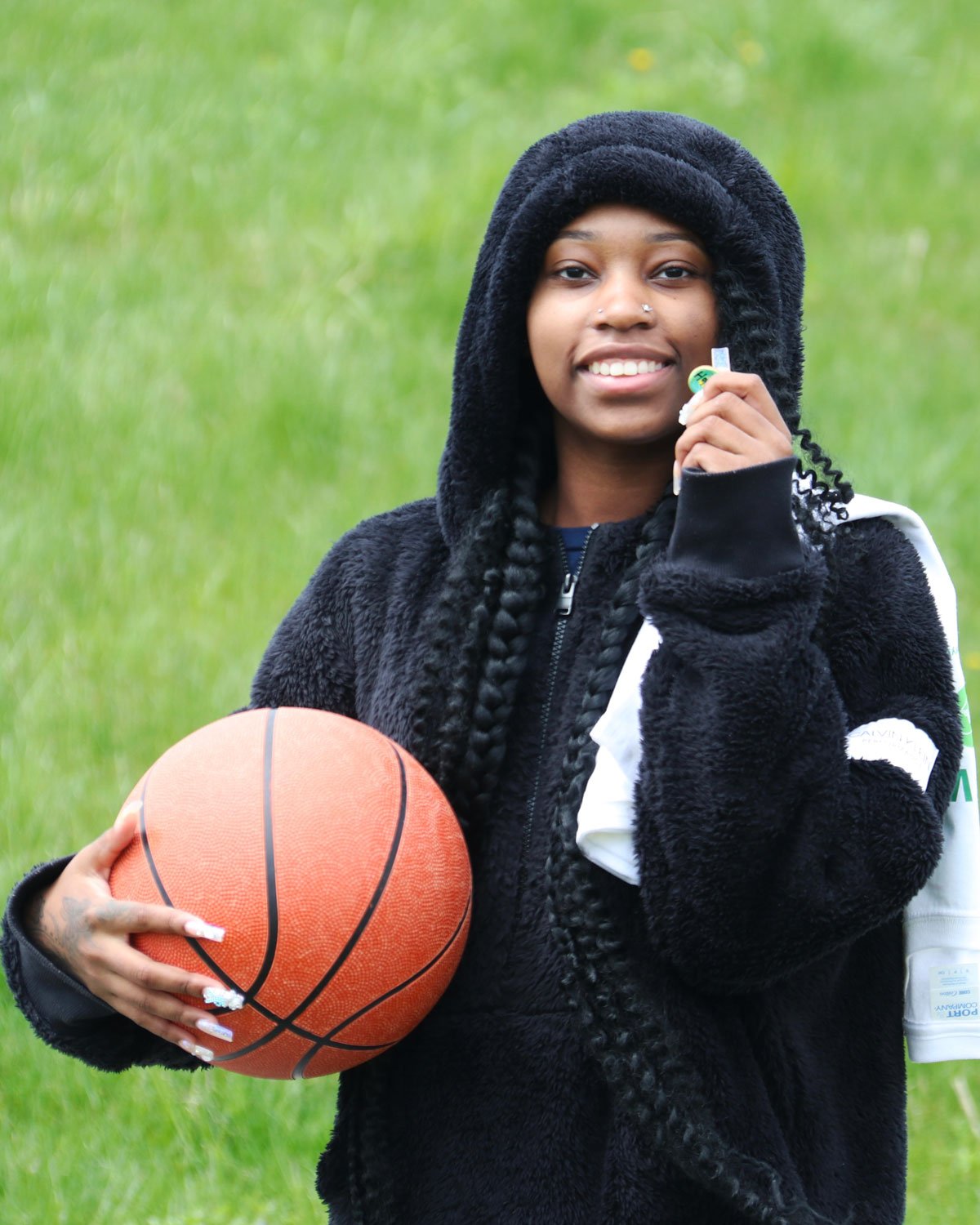 Young woman outdoors on a grass field holding a basketball and a key, smiling at the camera.