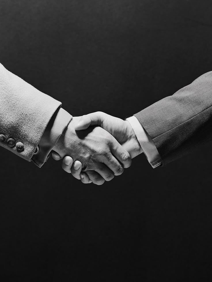 Black and white image of two people shaking hands, both wearing suits.