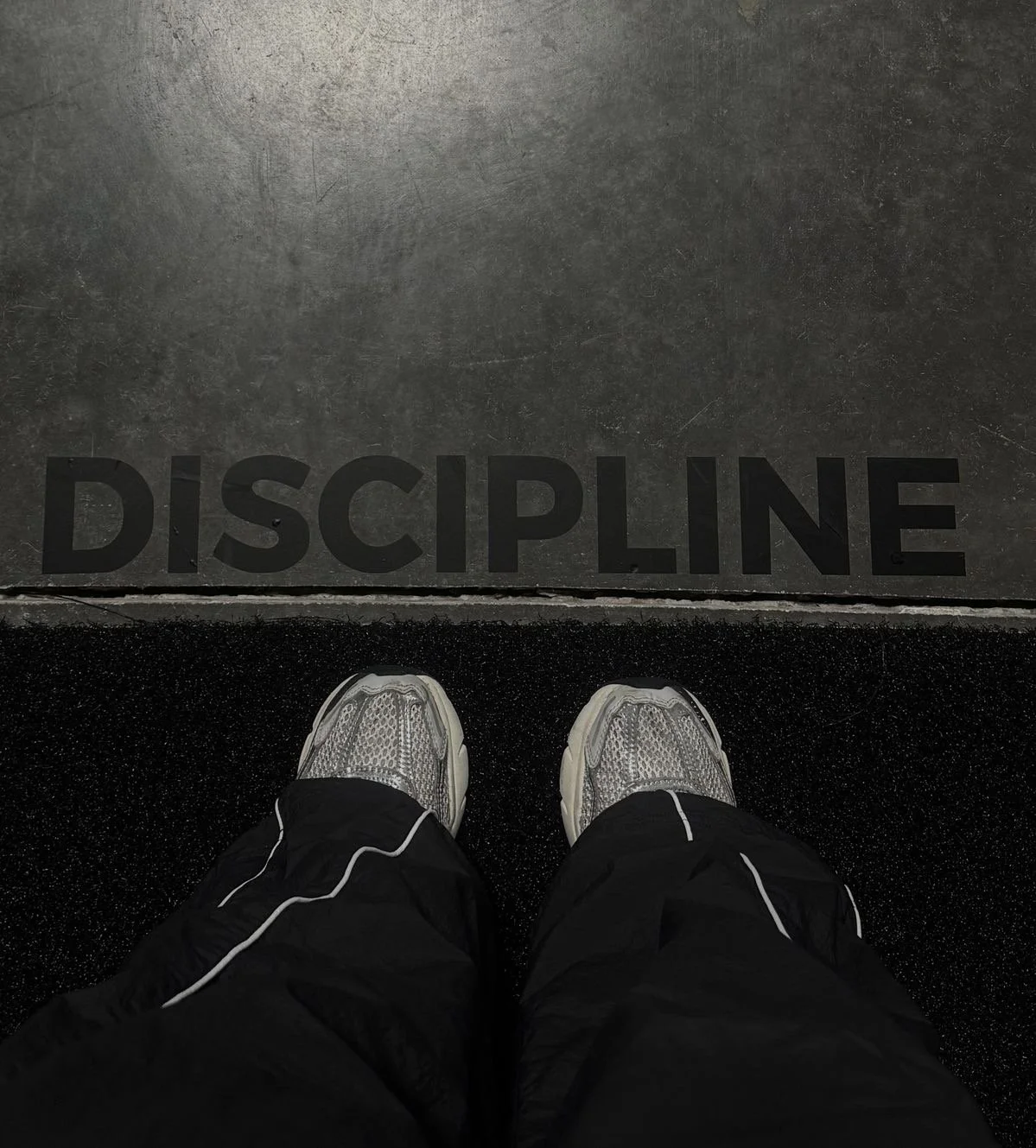 Overhead view of a person standing on a black mat in front of a gray wall with the word 'DISCIPLINE' written on it in large black letters.