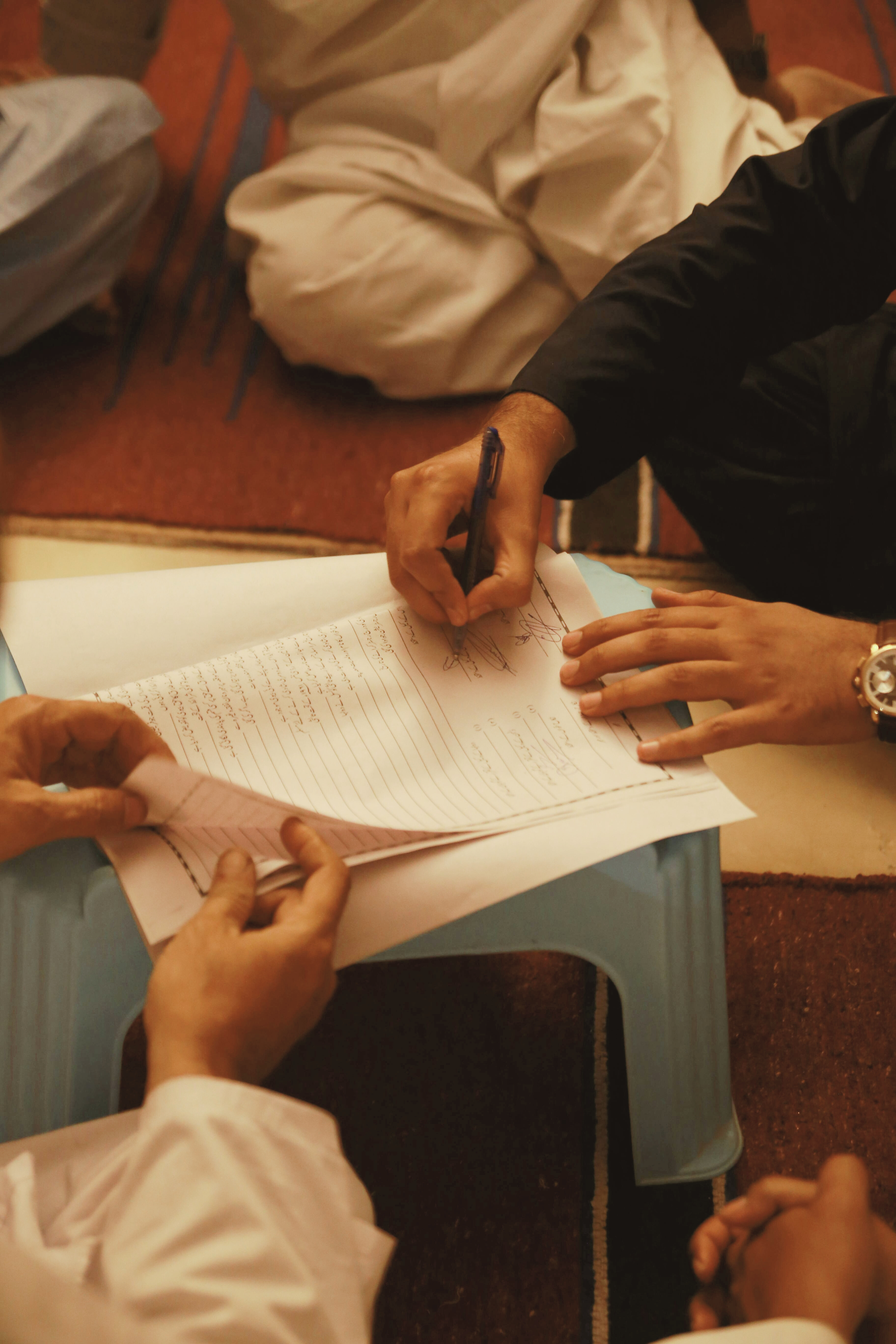 Multiple hands, one hand with a pen filling out a form that is an important document.